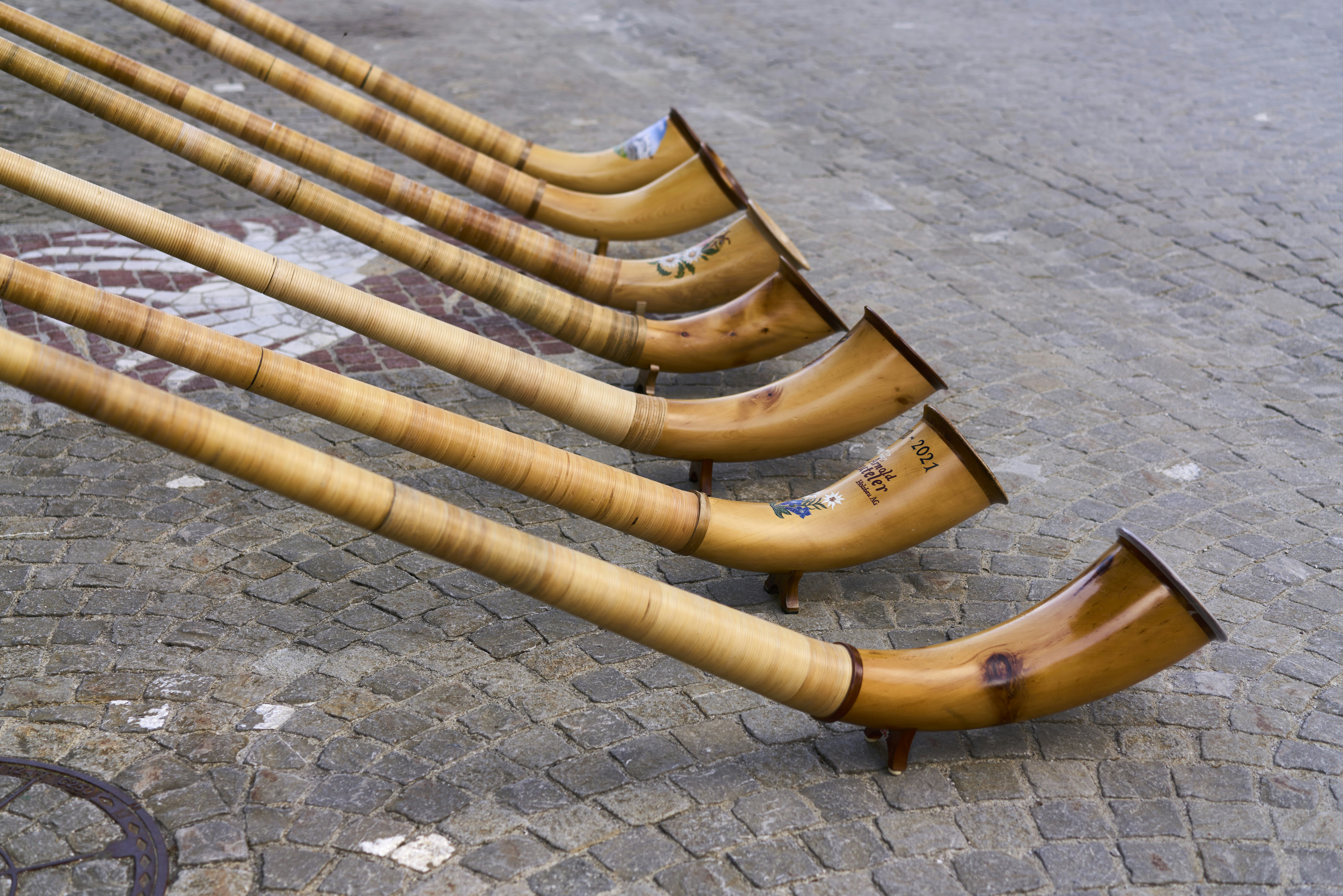 Vários longos alphorns de madeira repousando sobre um chão de paralelepípedos.