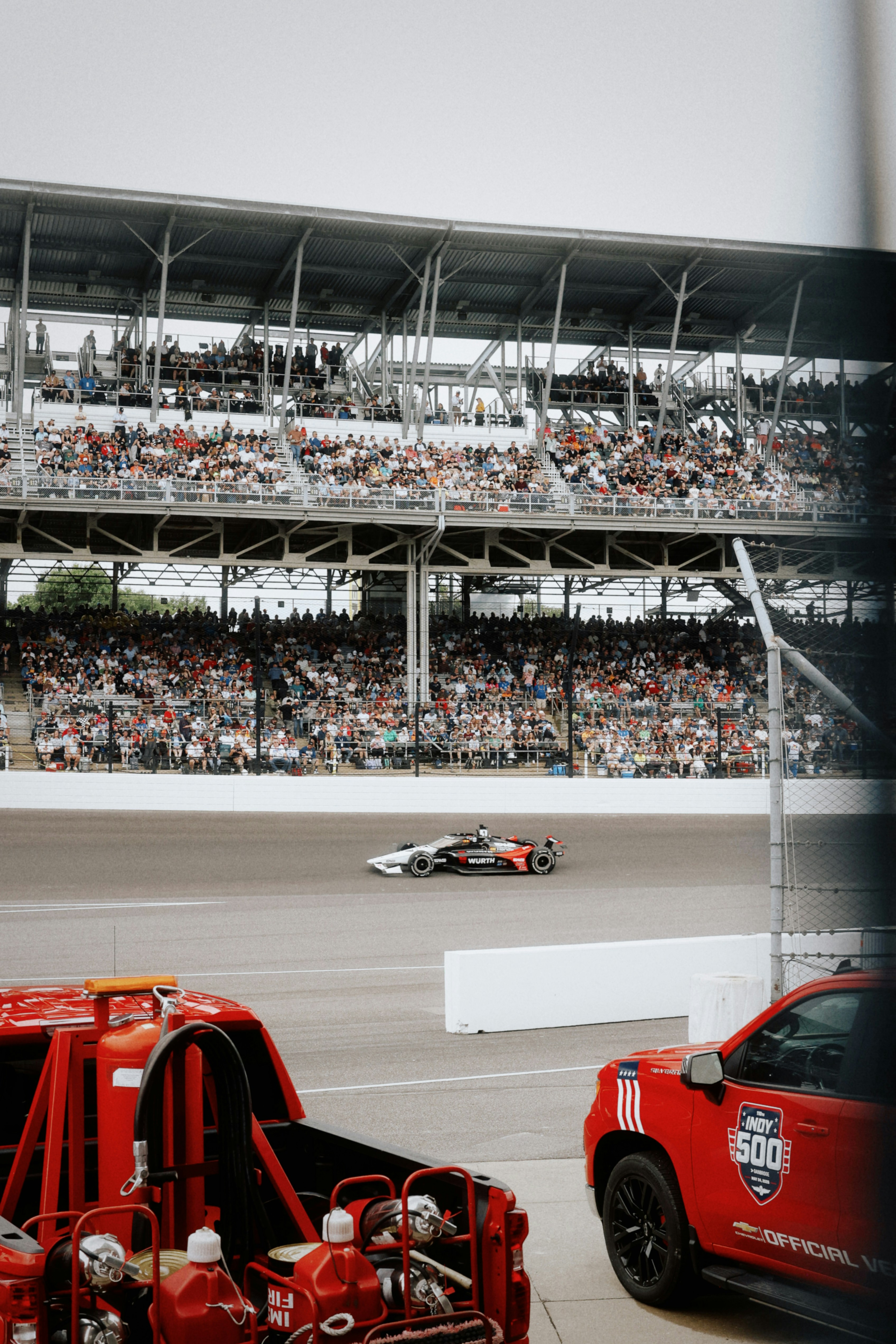 A race car speeds past grandstands filled with cheering spectators.