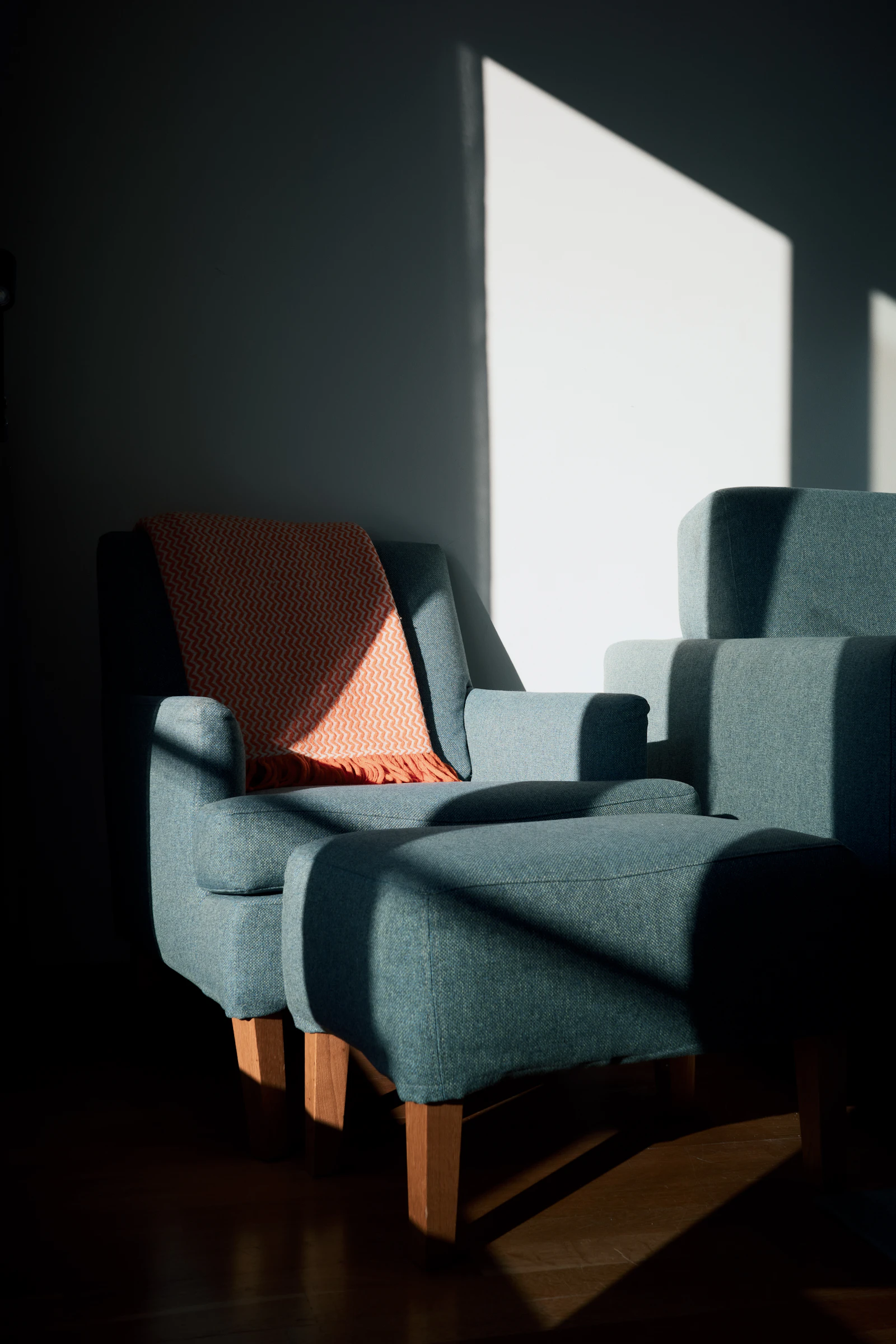 An armchair and ottoman with a blanket lit by morning sunlight