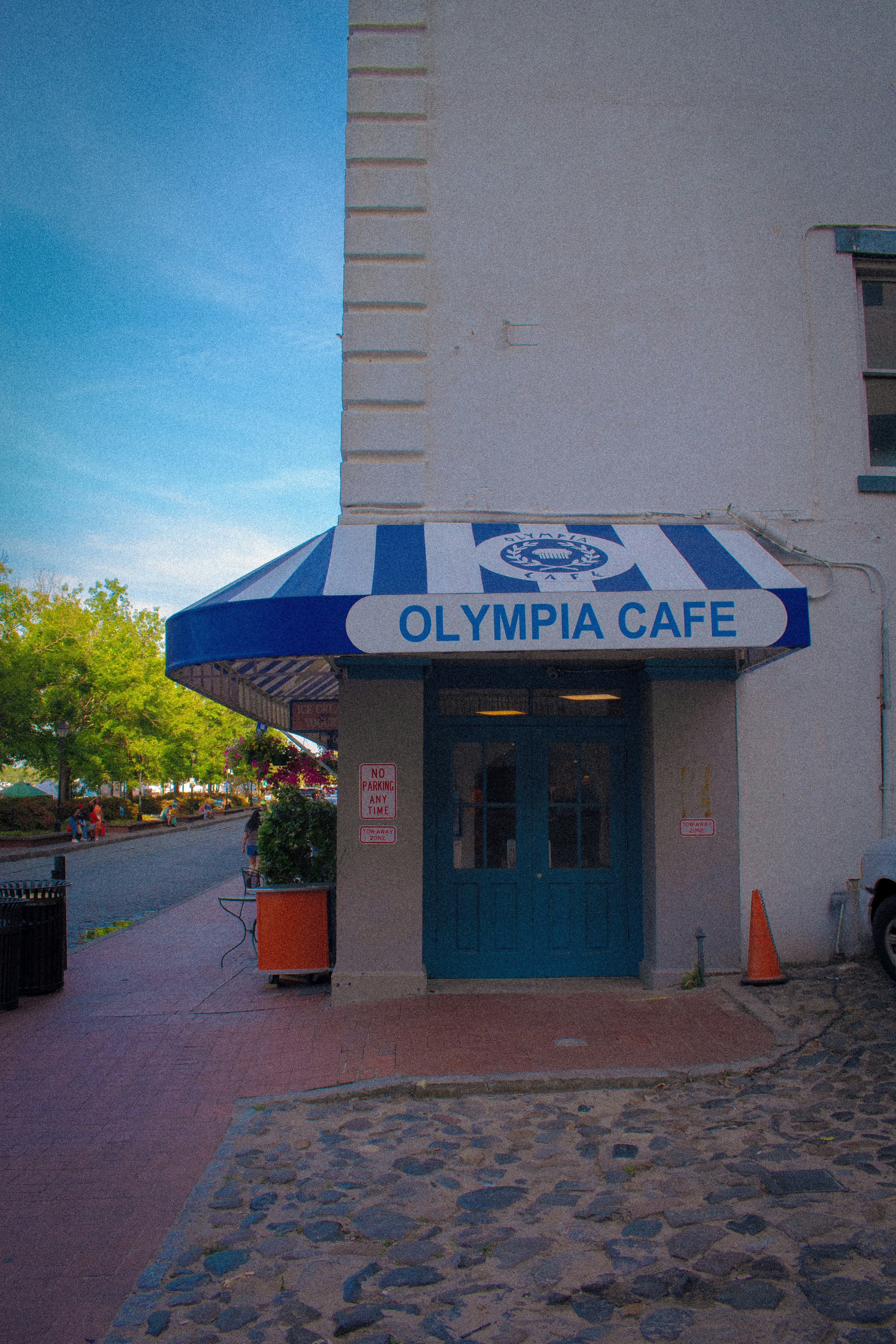 Olympia cafe entrance with blue awning and cobblestone street.