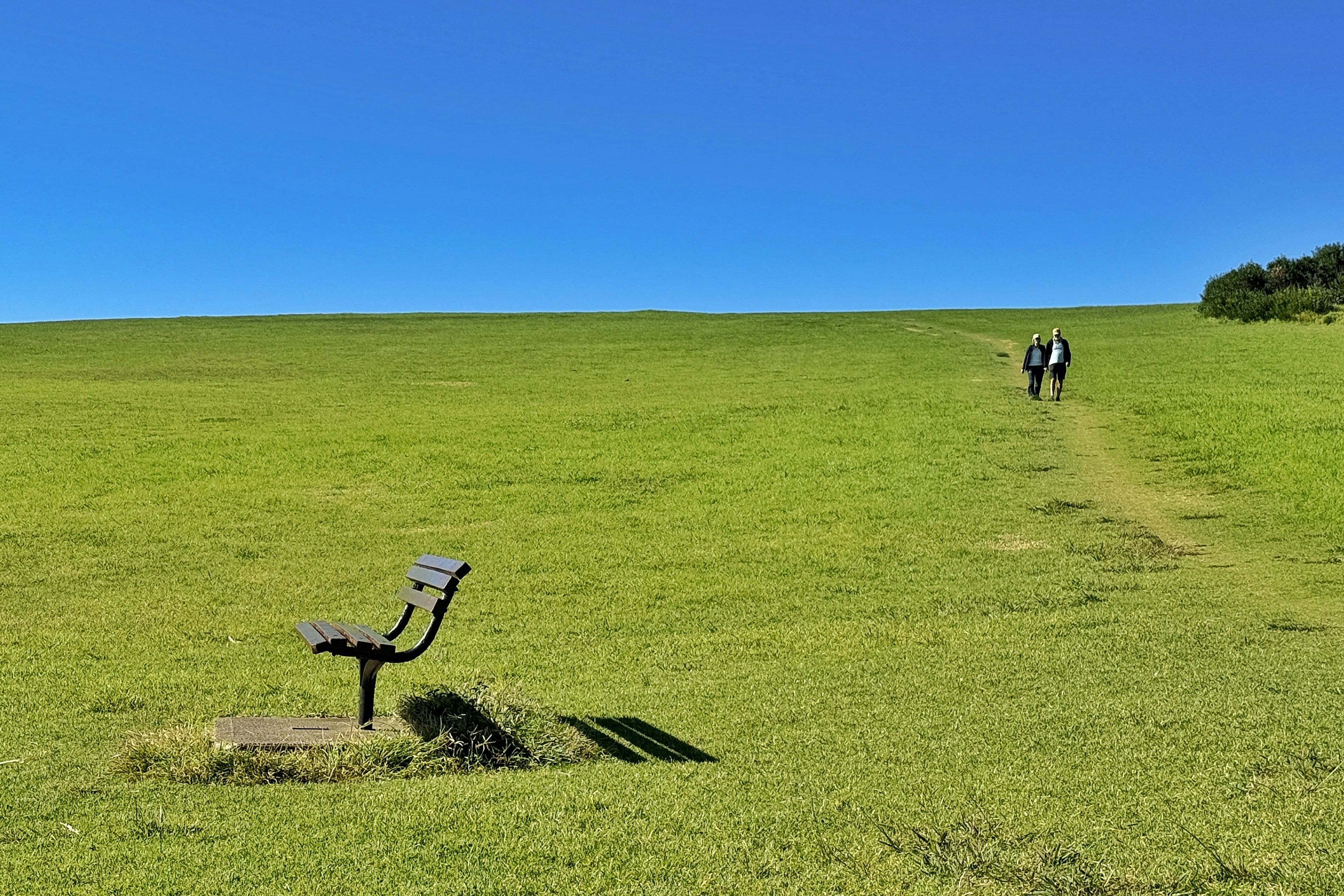 People walk up a grassy hill past a bench.