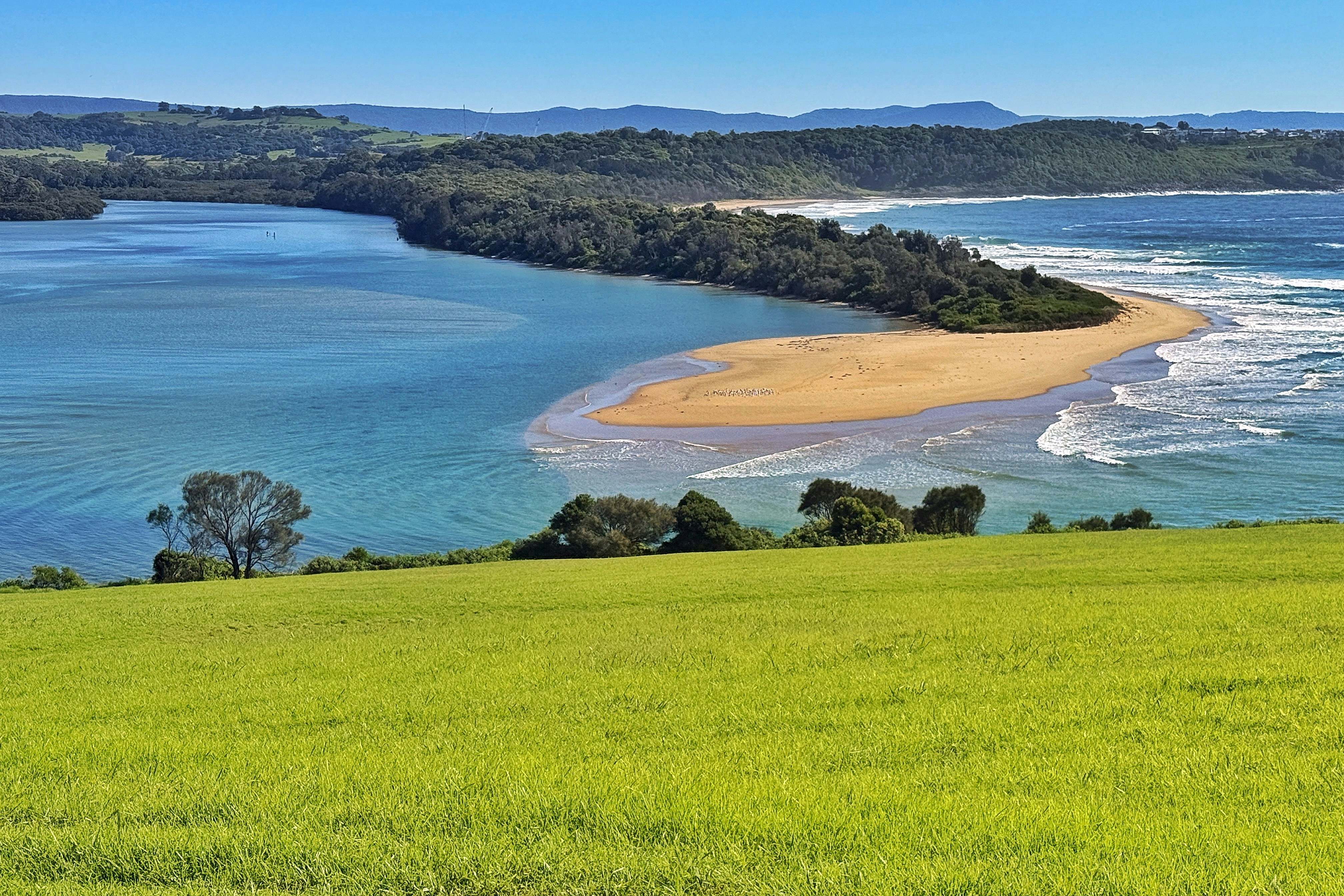 Lush green field overlooking a coastal river mouth and ocean.