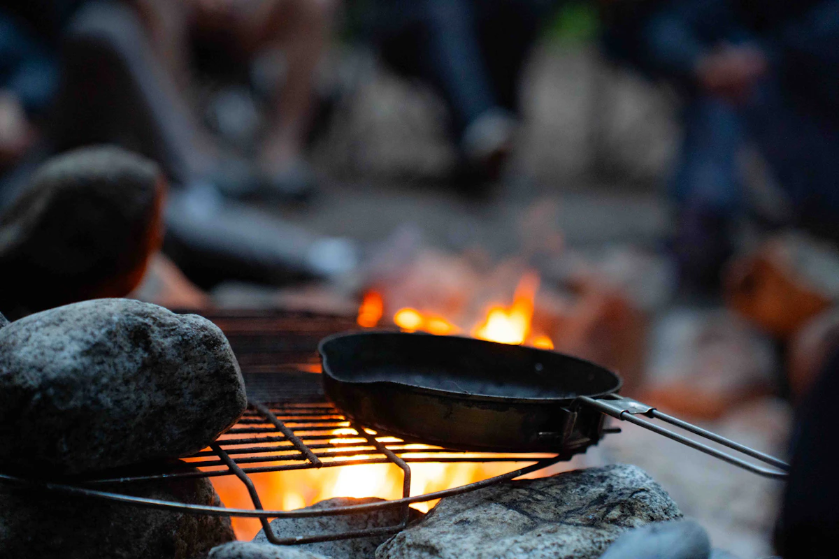 A cast-iron skillet heating on a grate over the campfire as the crew settles in at dusk
