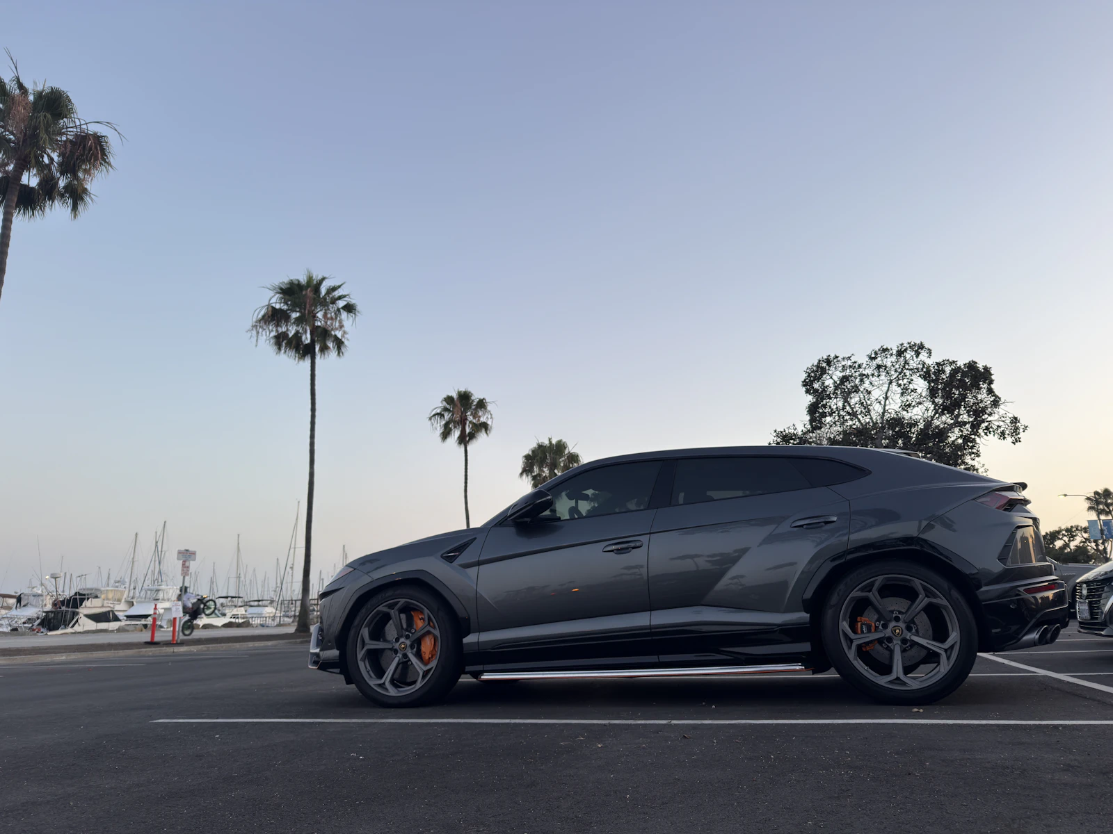 Grey Lamborghini Urus parked by a marina at sunset