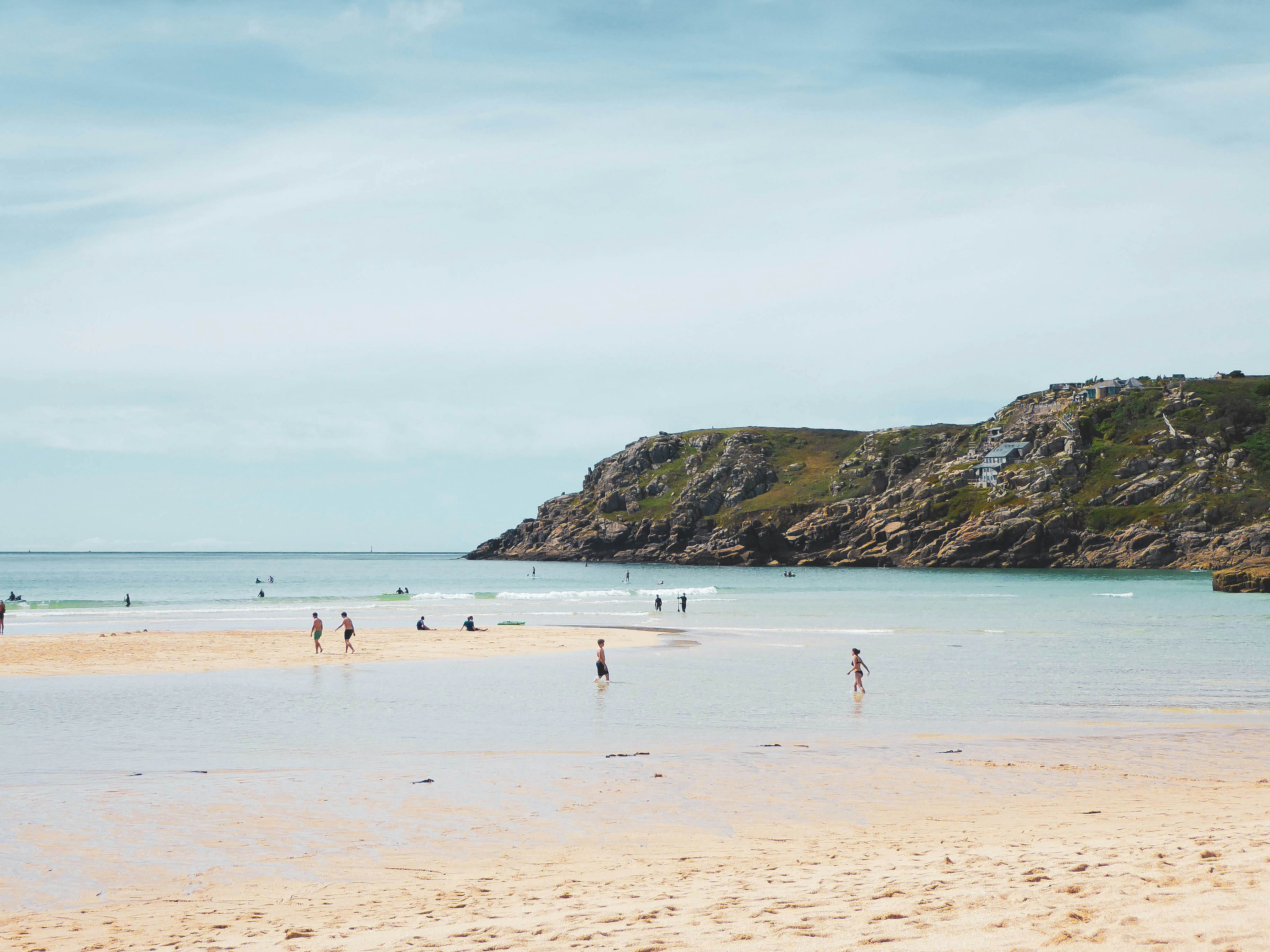 Des gens profitant d’une magnifique plage de sable avec un promontoire rocheux.