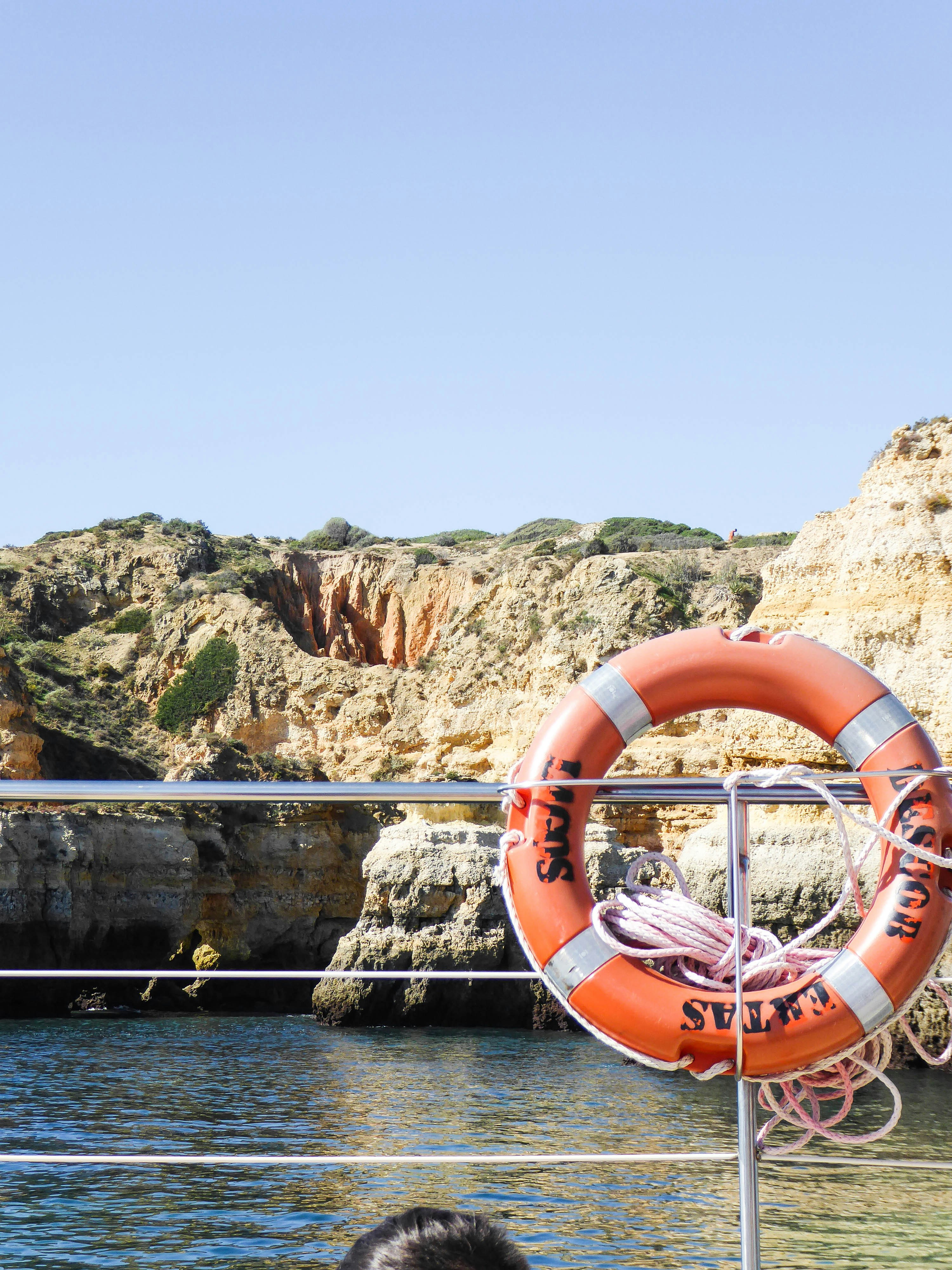 Bouée de sauvetage orange sur un bateau près des falaises rocheuses et de l’eau.