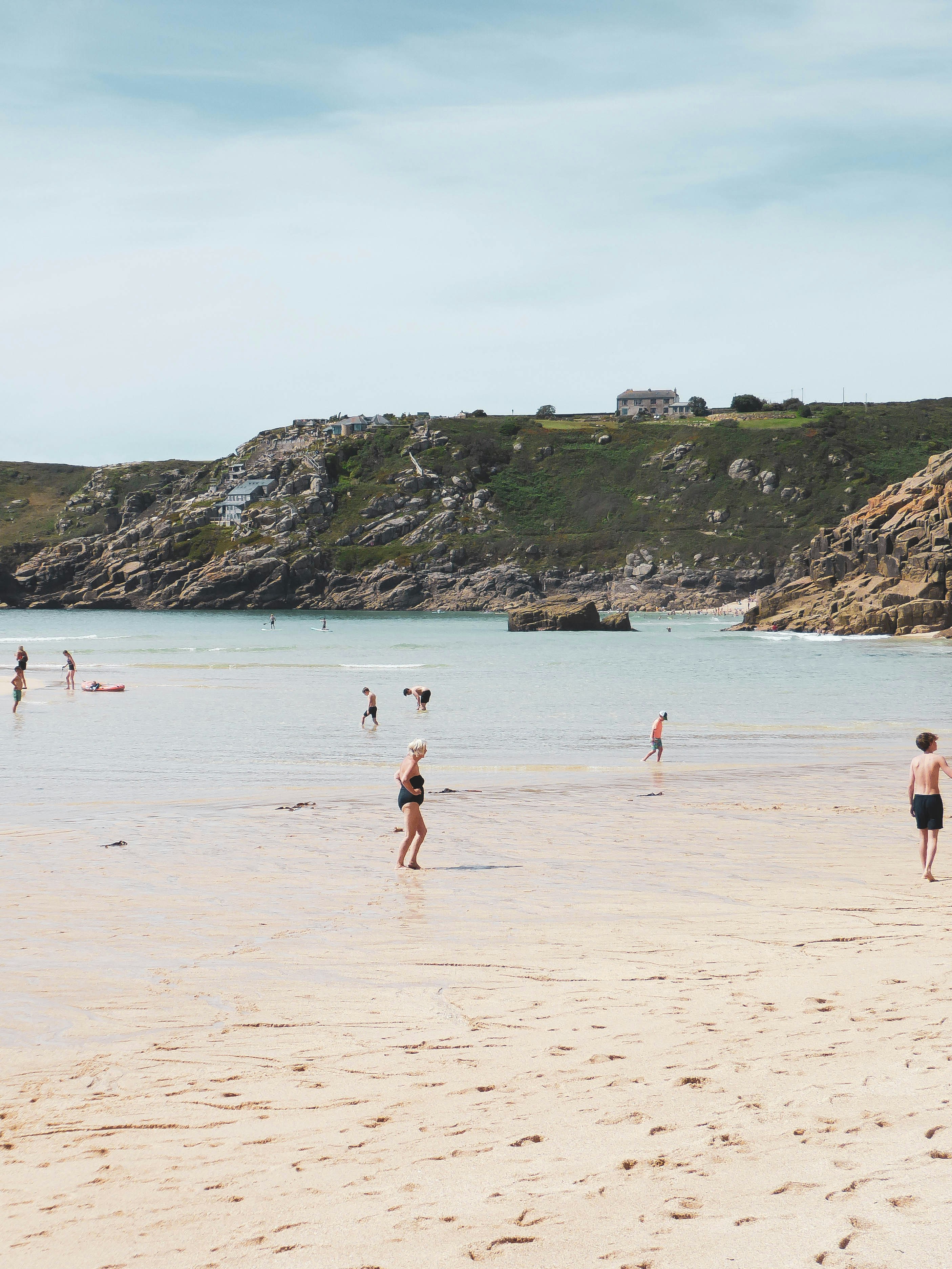 Des gens sur une plage à l’eau calme et aux falaises rocheuses.