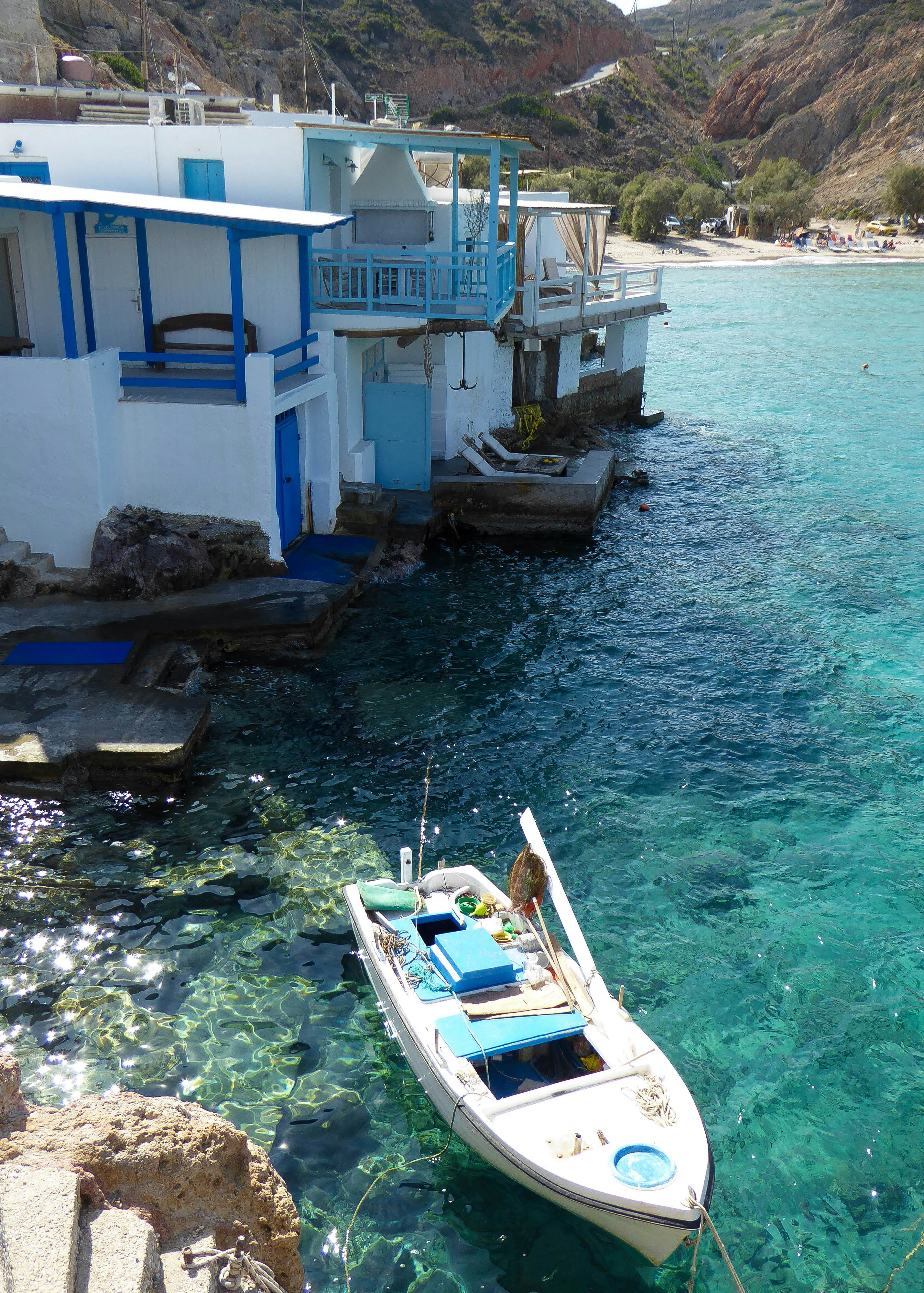 Bateau blanc amarré dans une eau bleue claire près de maisons en bord de mer.