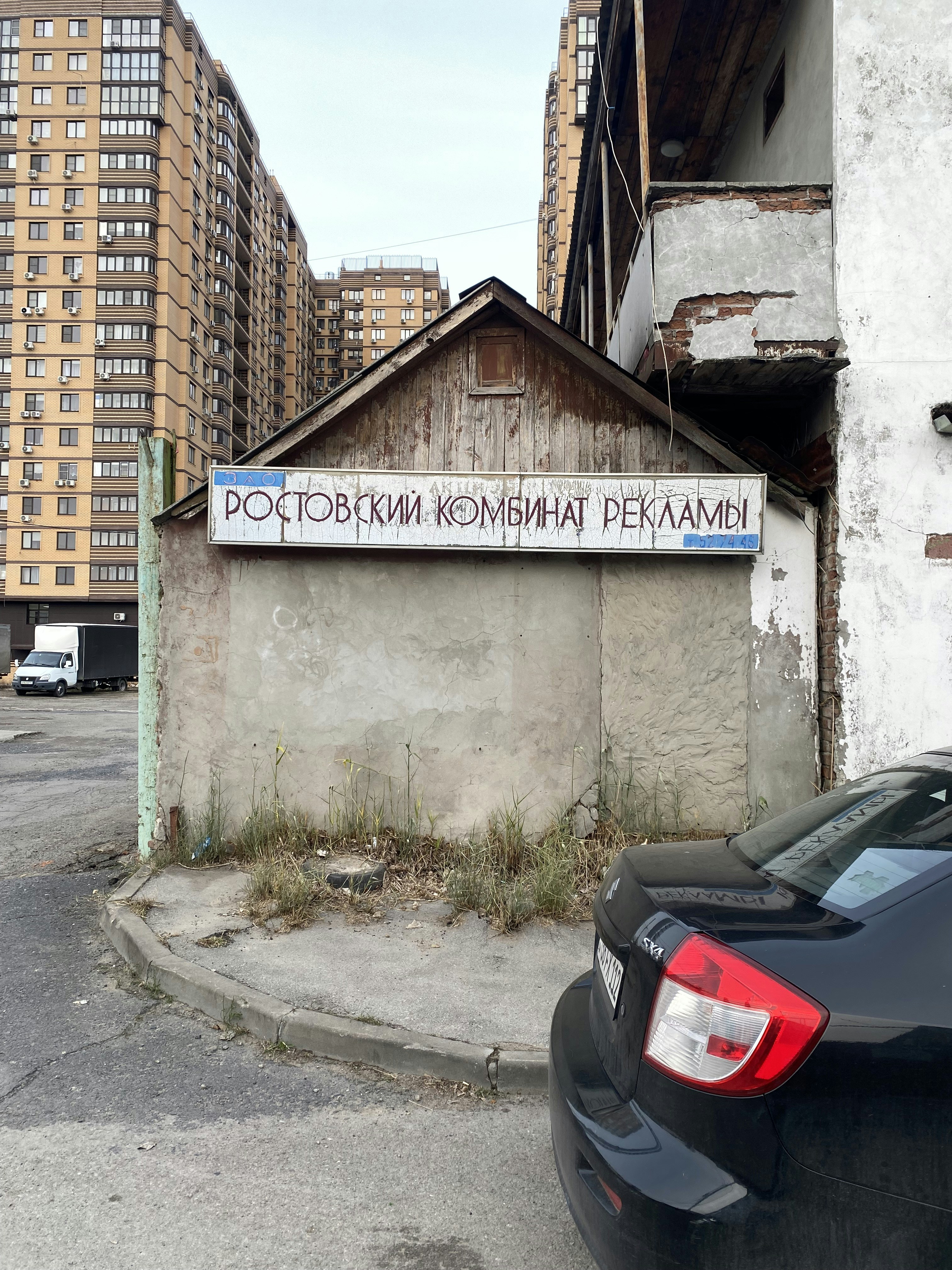 Weathered urban building with cyrillic sign, car, and apartments.