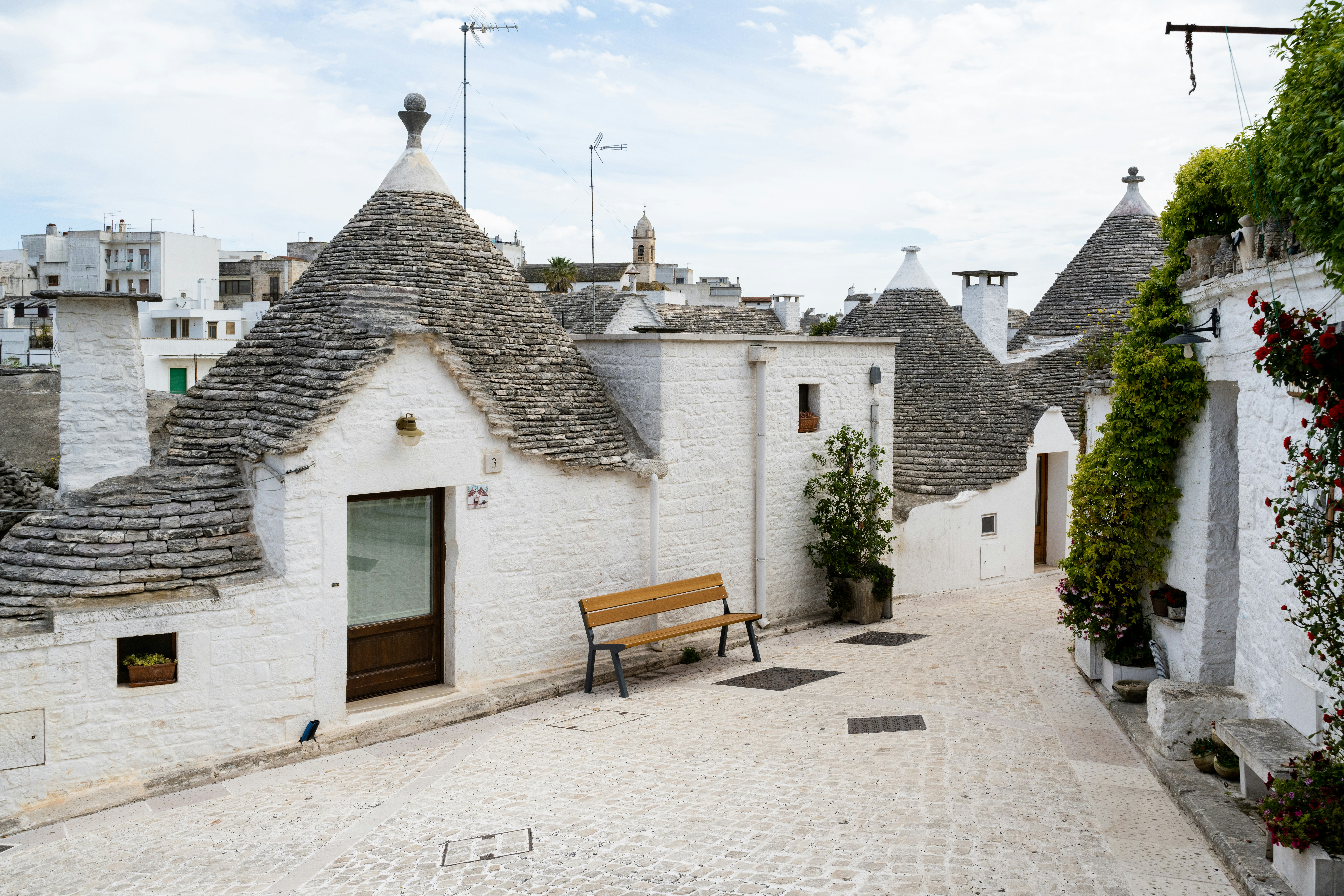 Whitewashed trulli with conical stone roofs and a wooden bench on a quiet street in Alberobello, Puglia, Italy