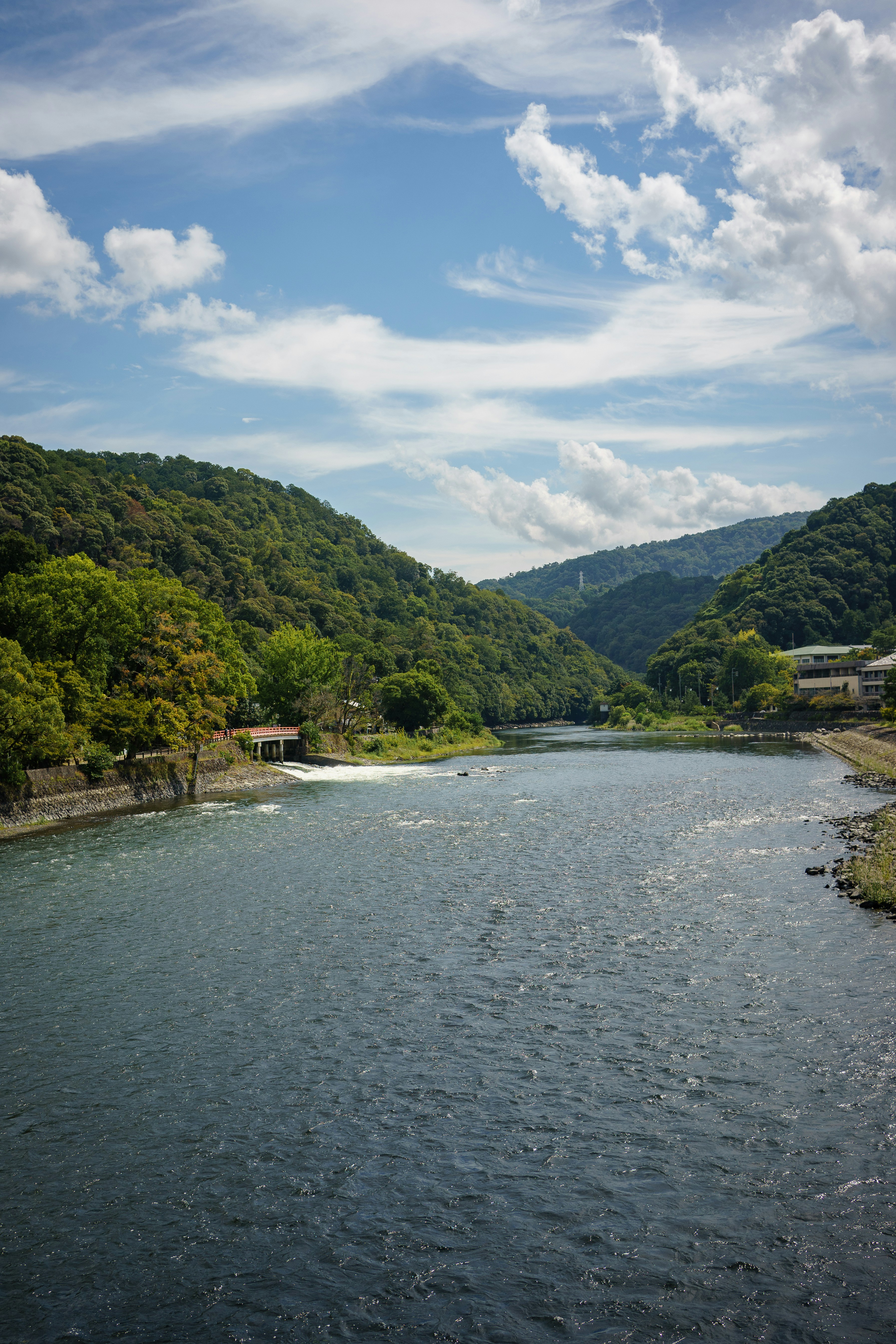 A river flows through green mountains under a blue sky.