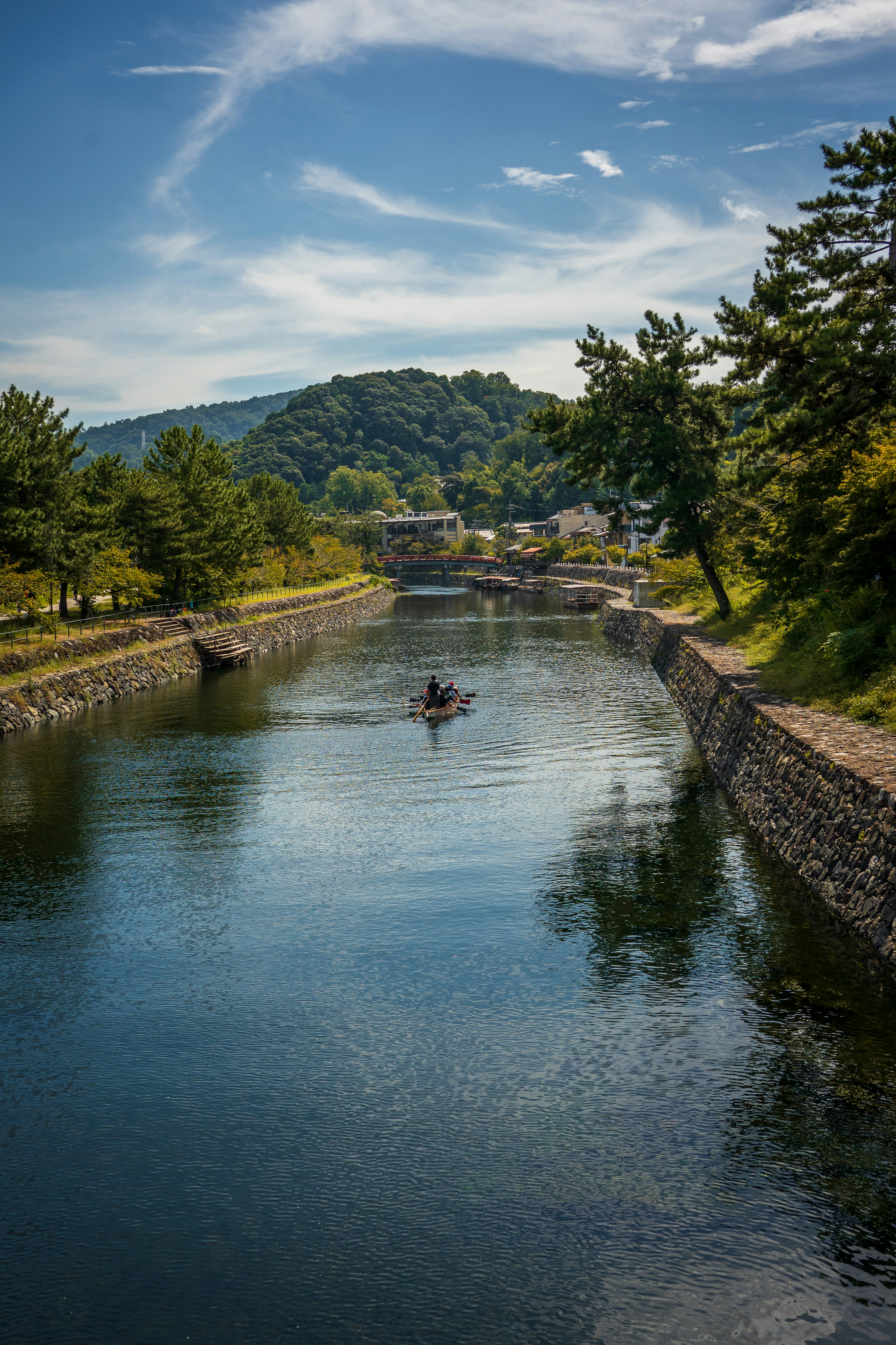 A person paddles a small boat down a serene river.