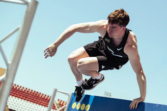 Young man vaults over a blue obstacle under clear sky.