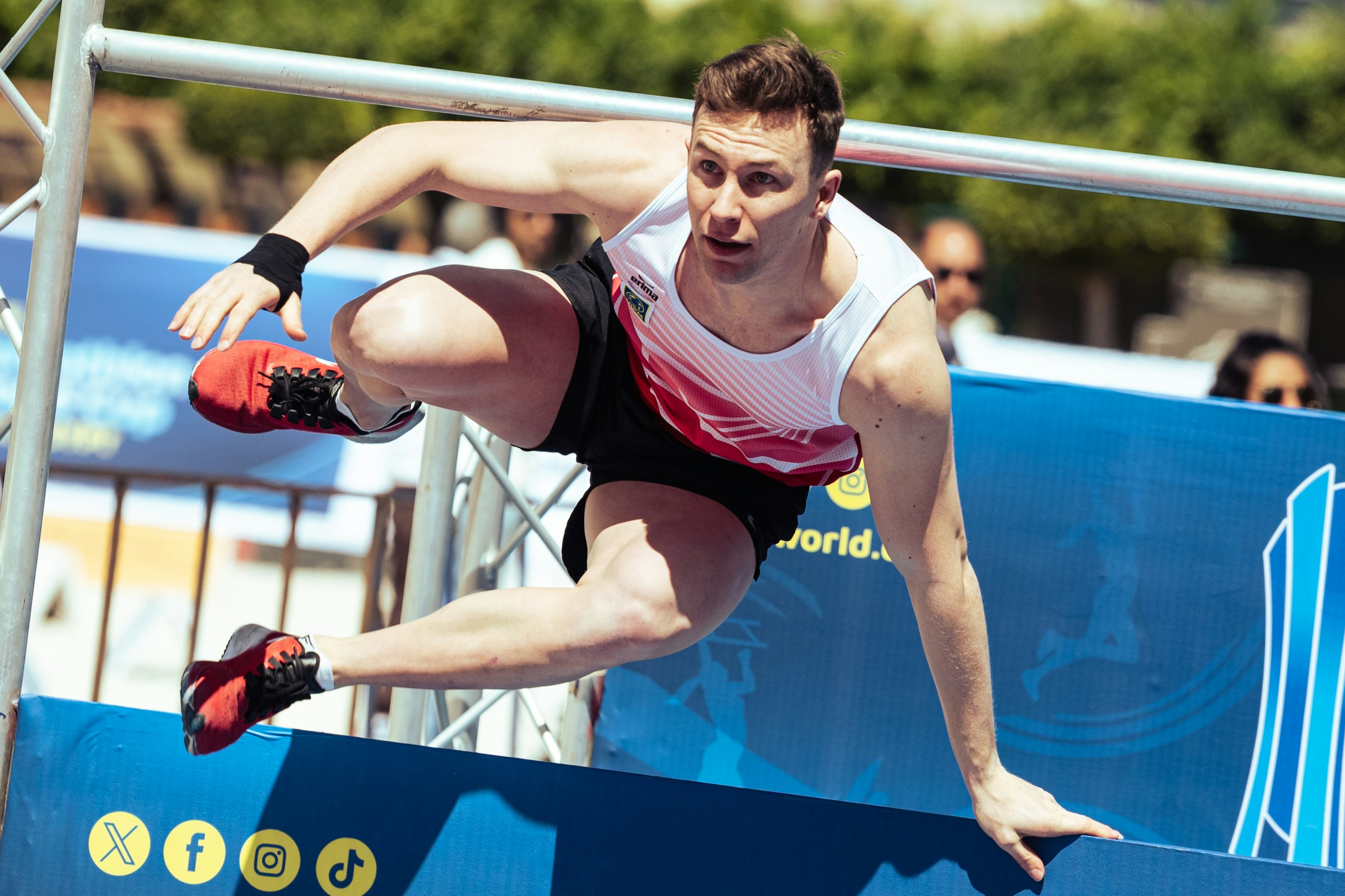 Man in athletic wear vaults over a blue obstacle outdoors.