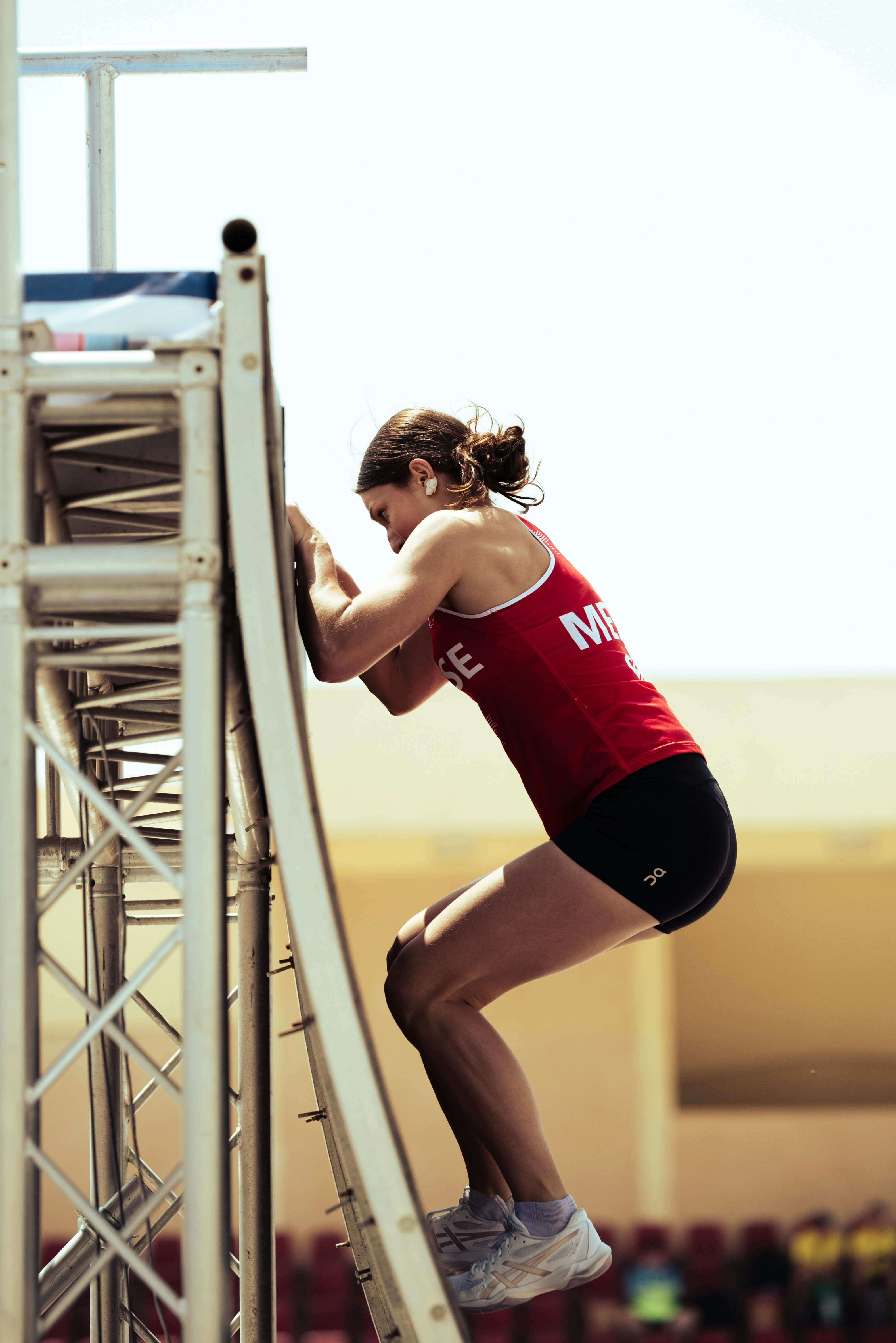 Athletic woman climbs a tall metal structure outdoors.