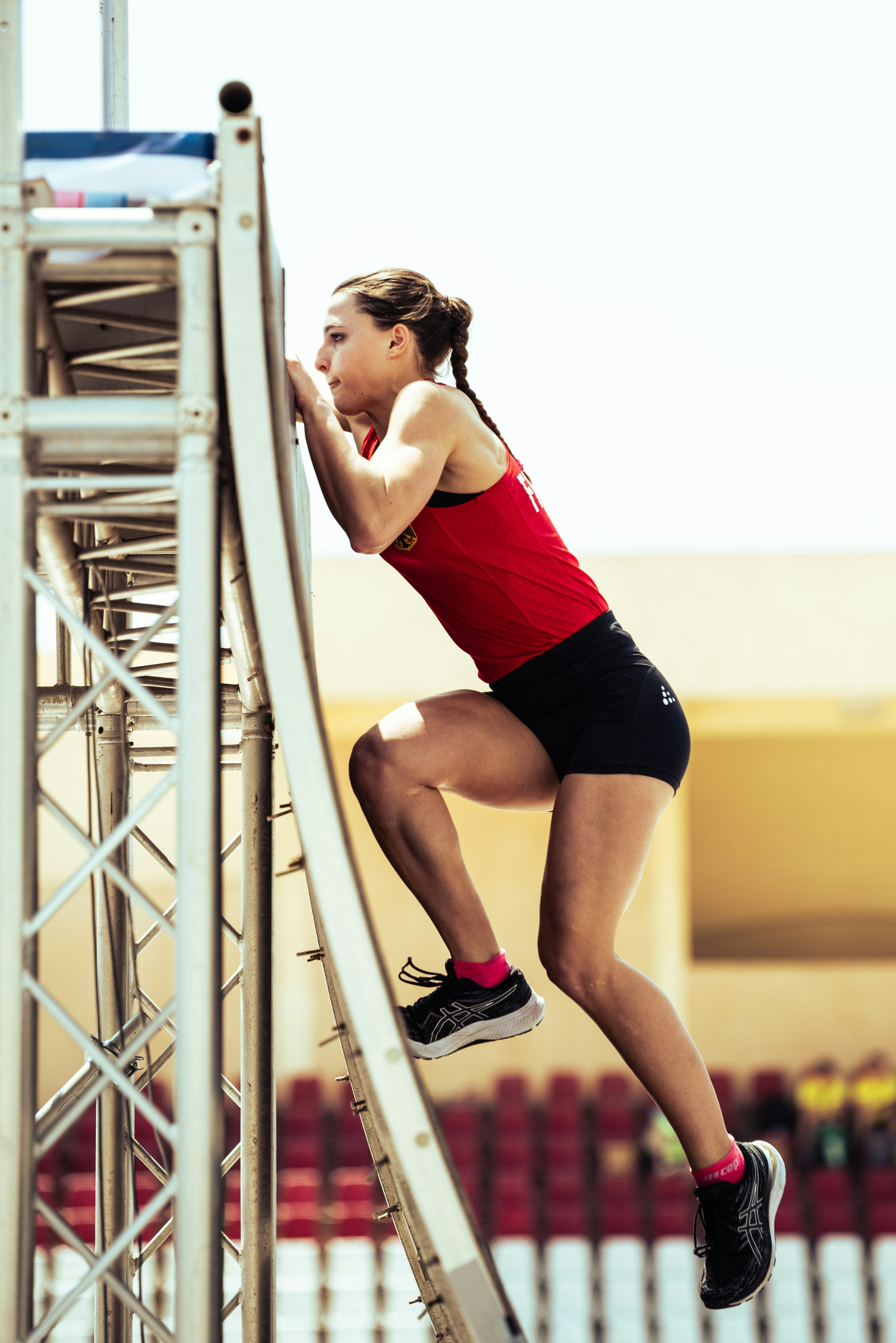 A woman in athletic wear climbs a metal obstacle course.
