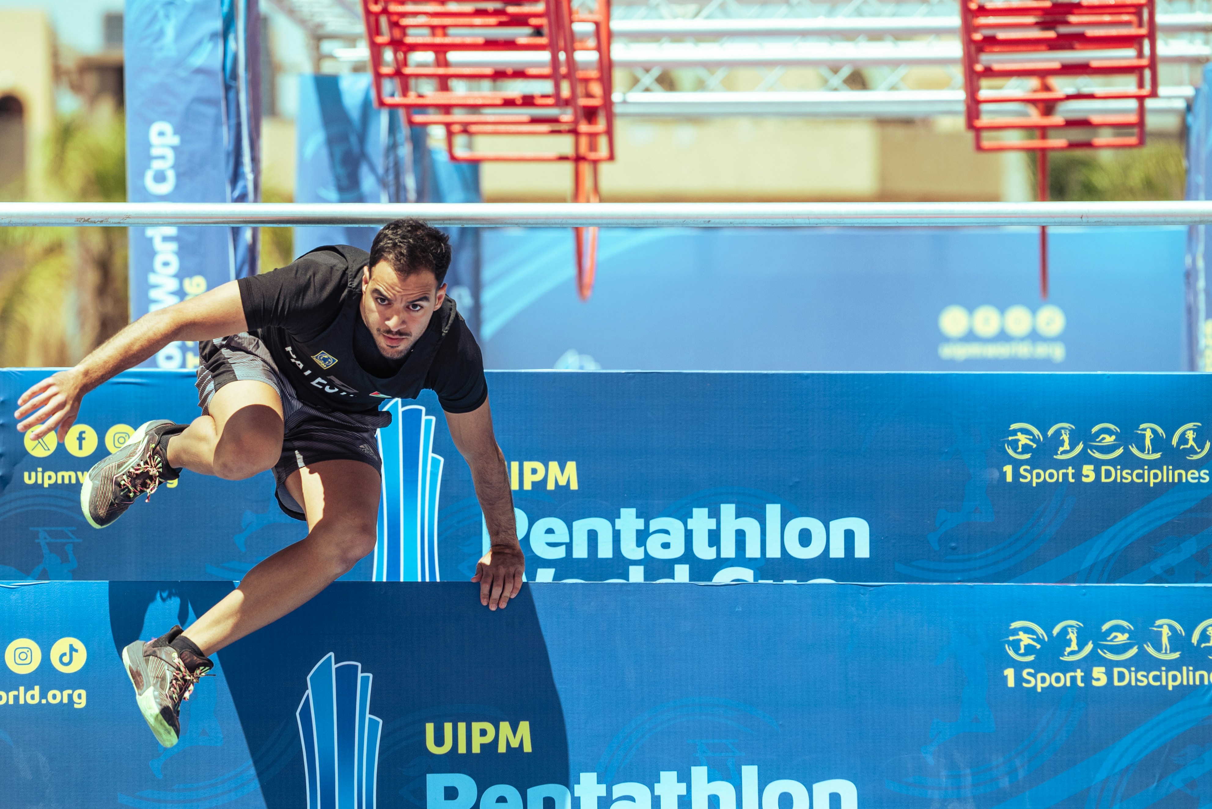 Atlet menavigasi rintangan biru dalam kompetisi pentathlon.