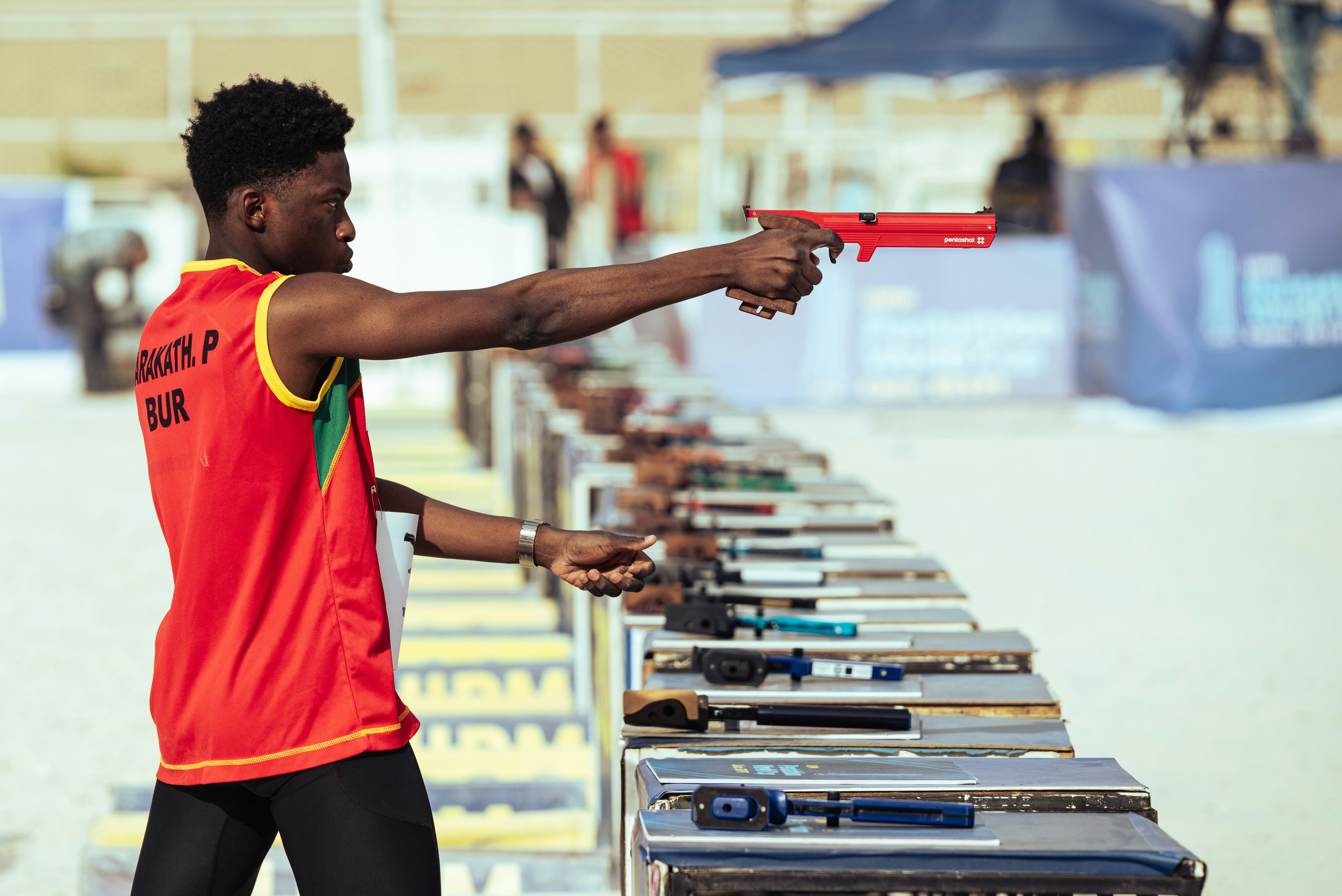 Atlet muda berlatih menembak dengan pistol merah di luar ruangan.