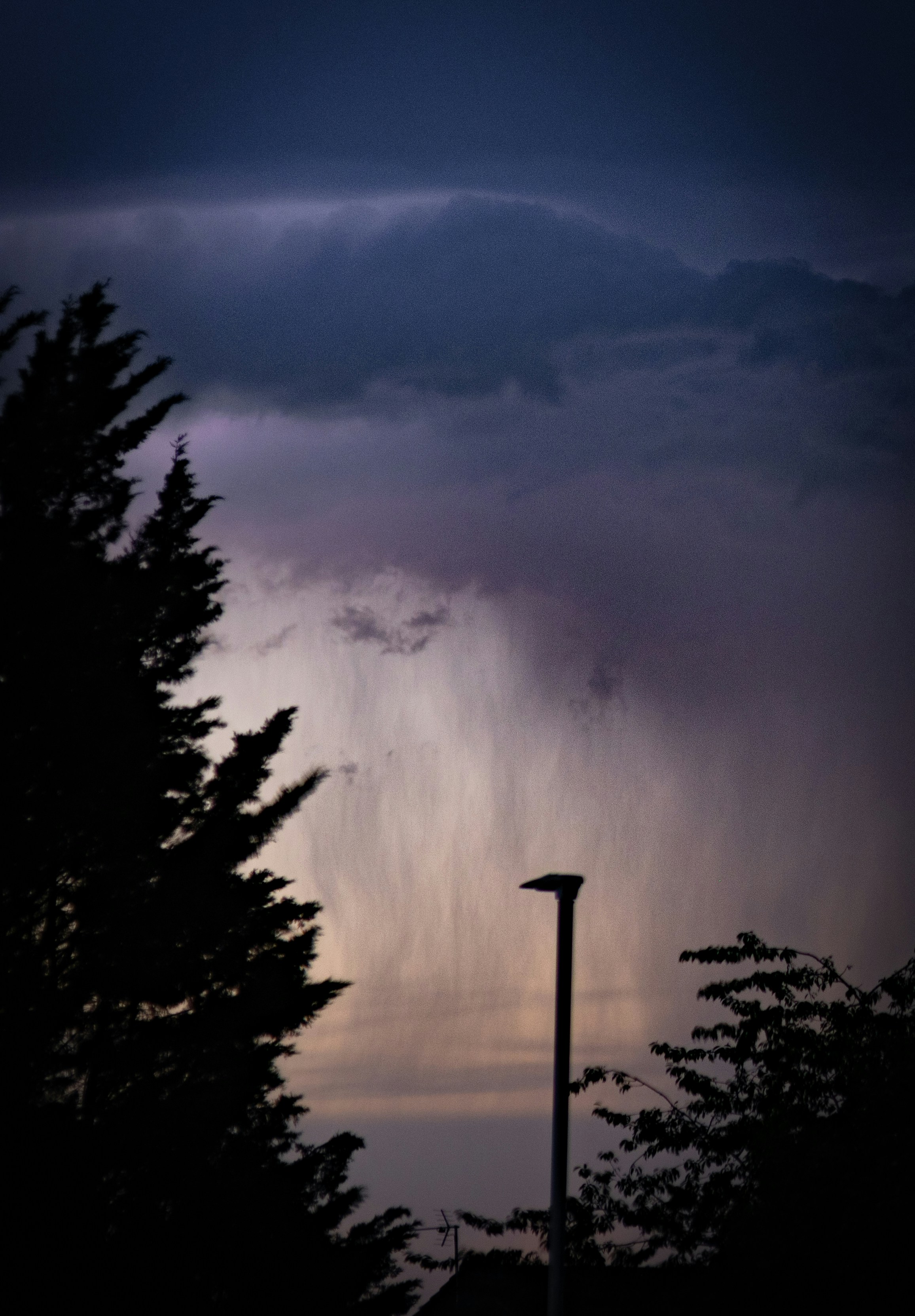 Heavy rain falling from dark storm clouds at dusk.
