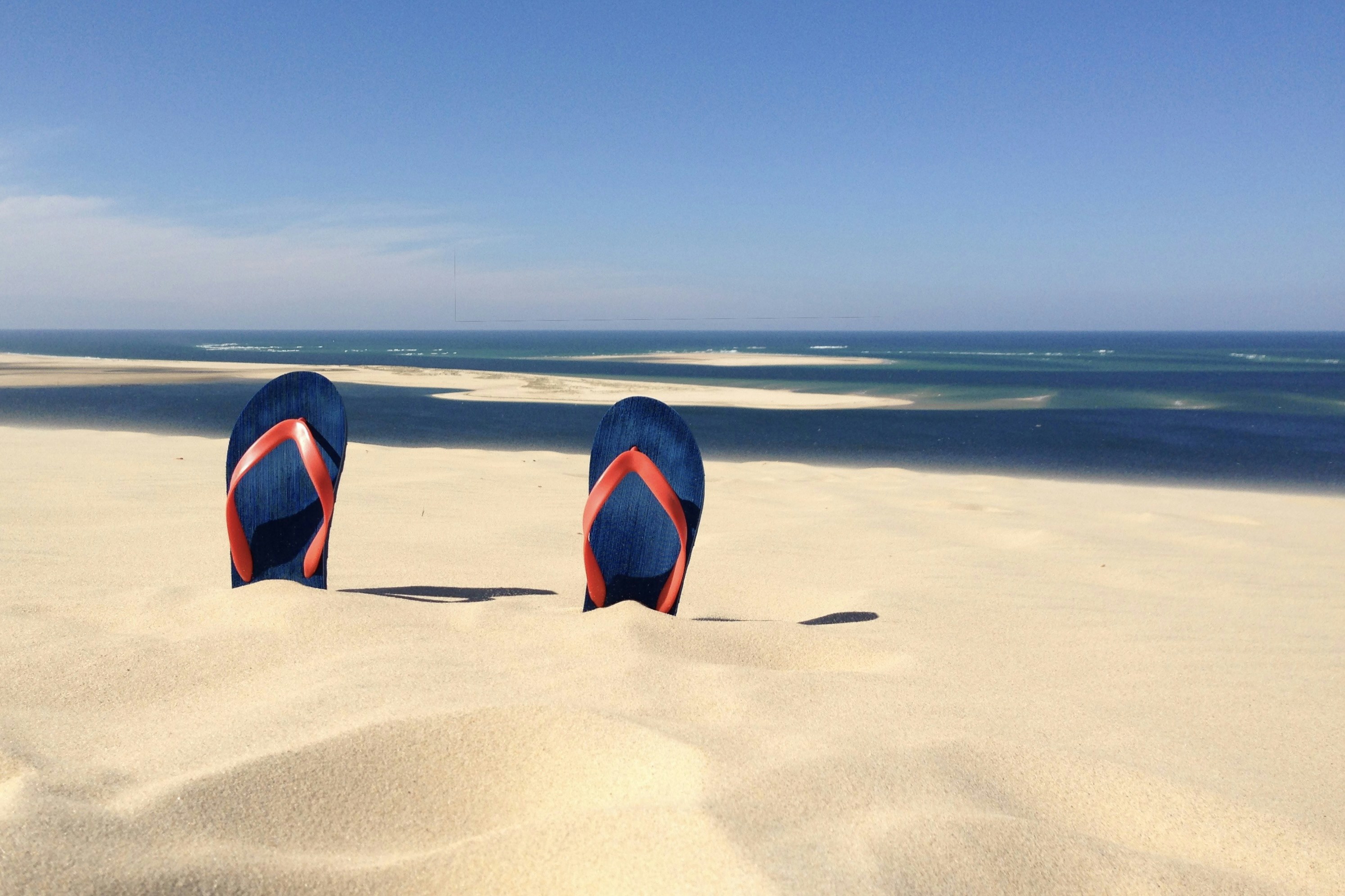 Flip-flops in sand with ocean and clear blue sky