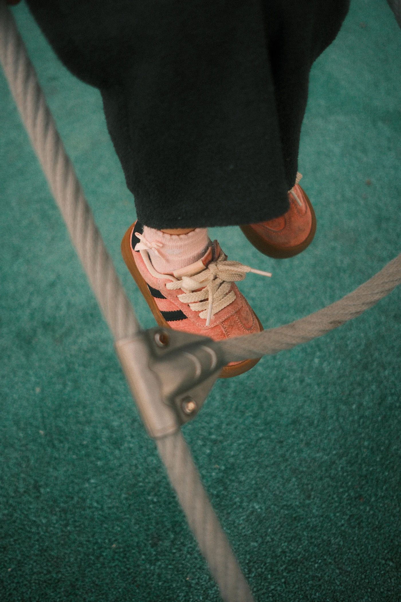 Child wearing pink sneakers while climbing on playground rope
