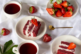 Red velvet cake slices, strawberries, and berry drinks on white.