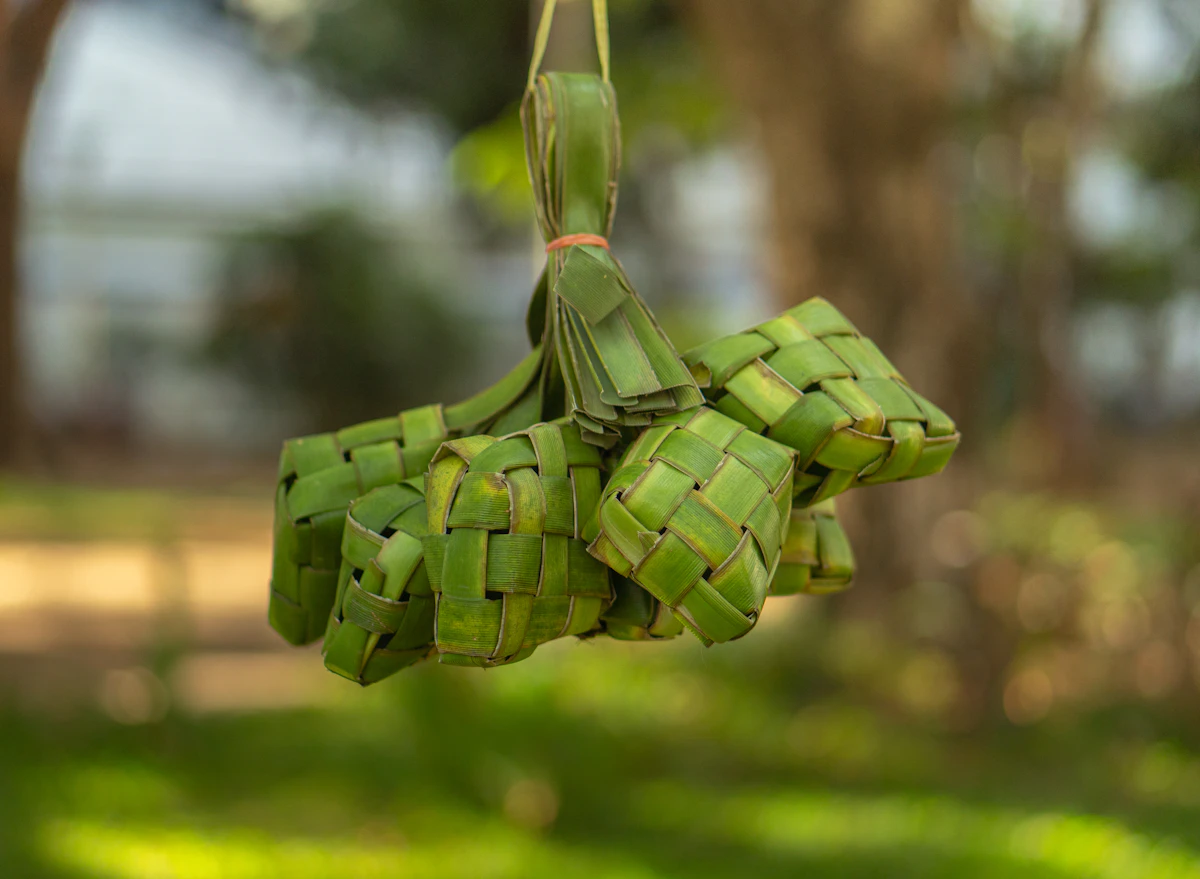 Green woven palm leaf ketupat pouches hanging outdoors