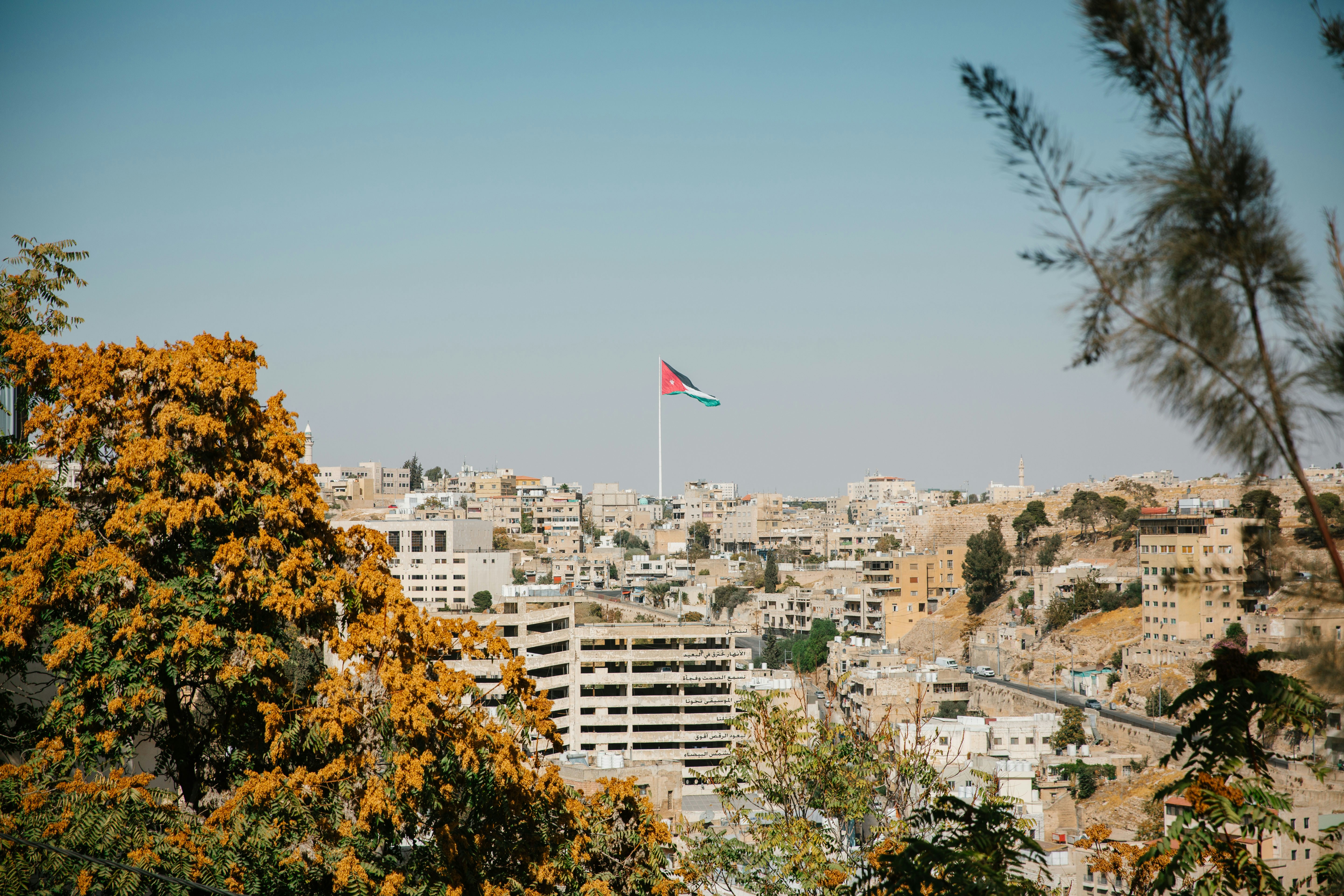 A bandeira jordaniana tremulha alto sobre uma cidade emoldurada por árvores.