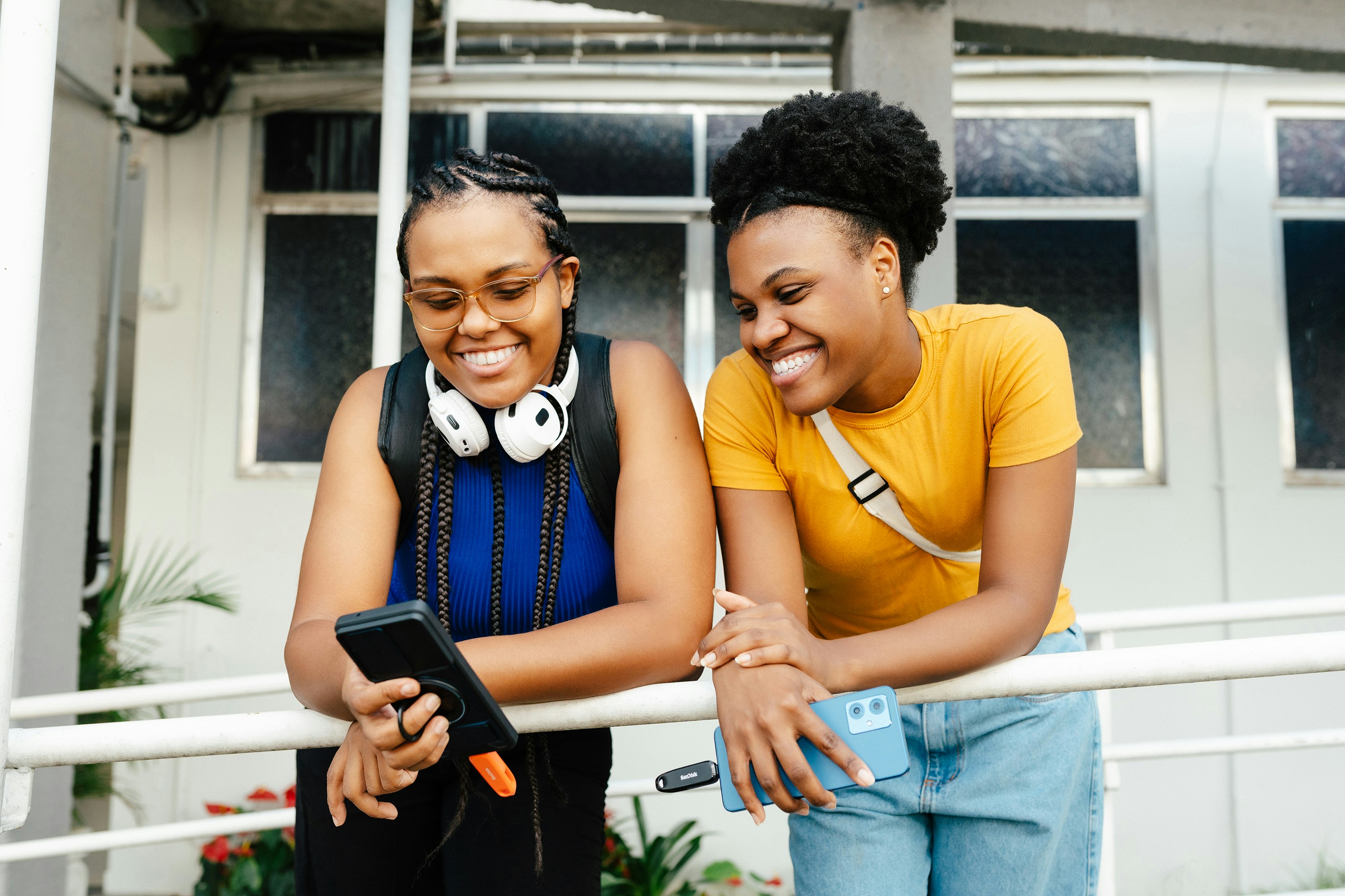 Two smiling women looking at a smartphone outdoors.