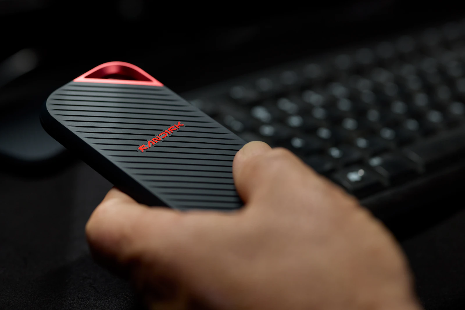 Hand holding a portable SSD next to a keyboard