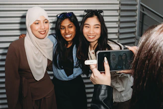 A person photographs three smiling women with a smartphone.