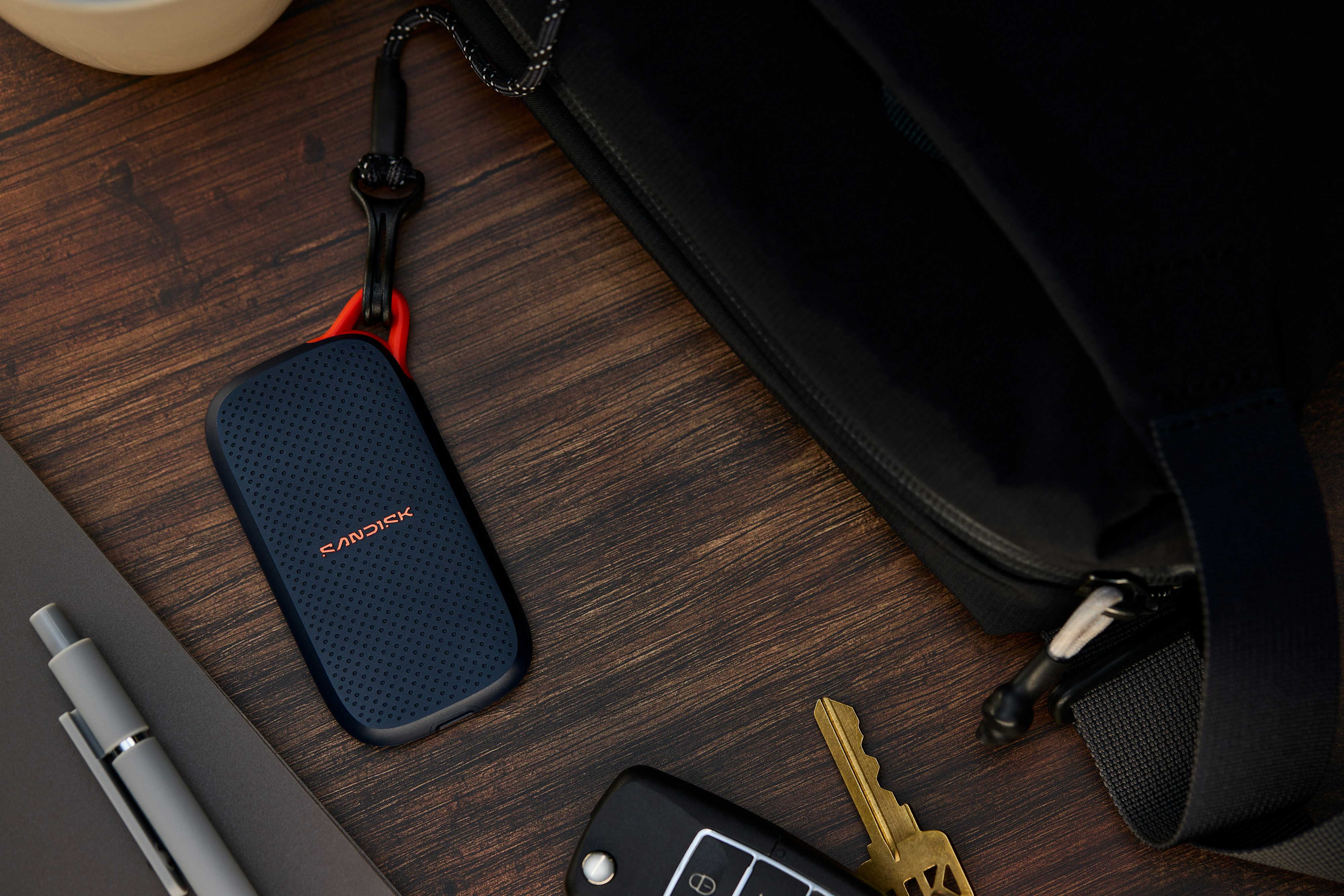 Portable ssd, keys, and pen next to a black bag.