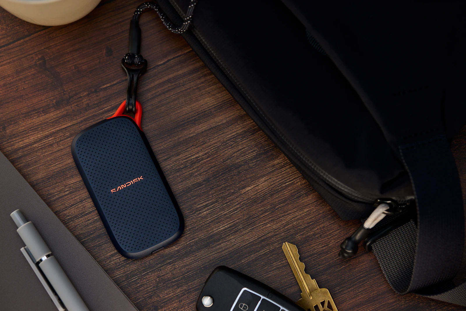 Portable solid state drive beside a bag, keys, and desk accessories