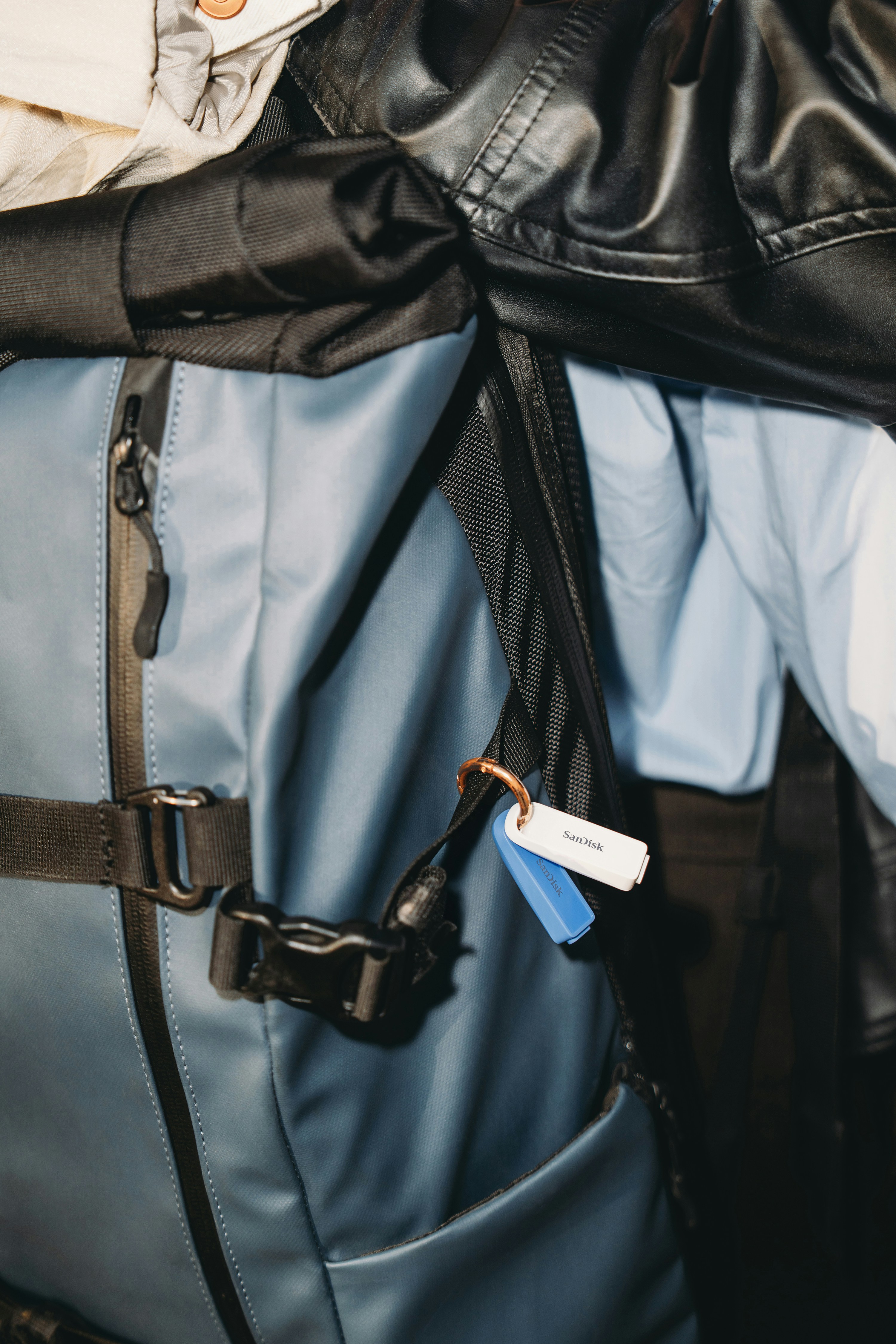 A blue backpack with keys and jackets hanging from it.