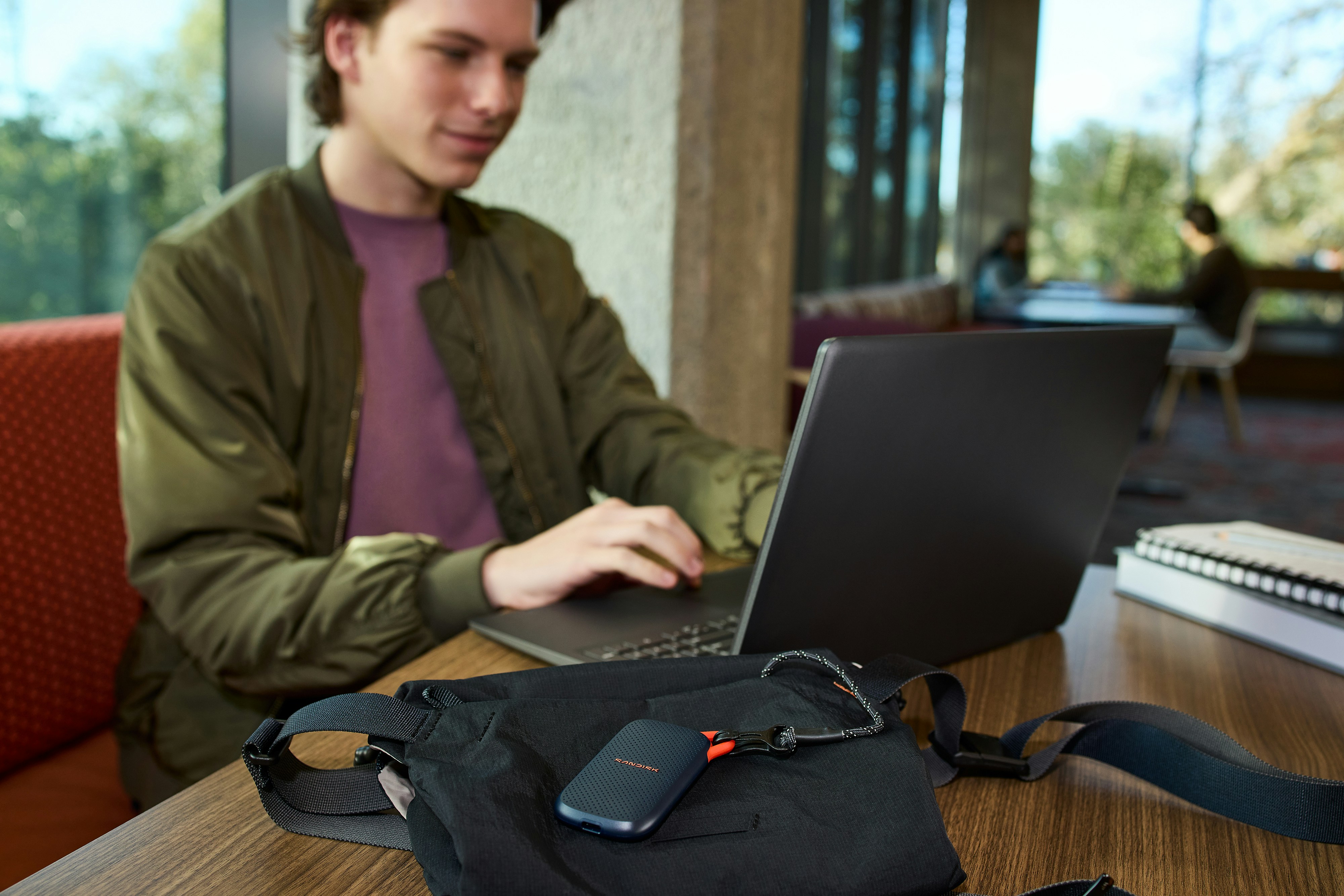 Pemuda menggunakan laptop, perangkat penyimpanan portabel di atas meja.