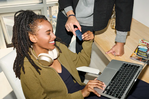 Smiling woman uses laptop, person holds credit card nearby