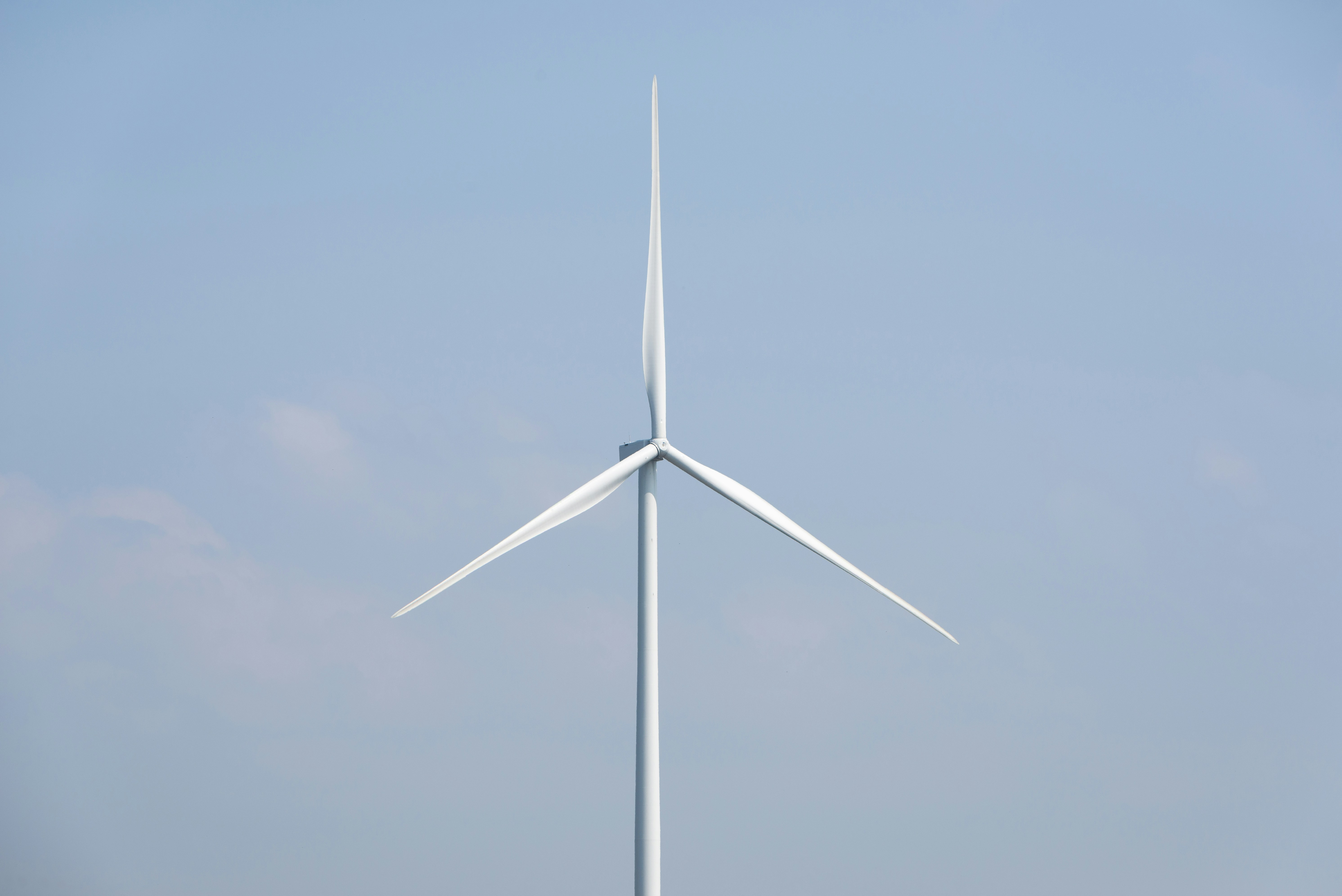 A white wind turbine stands tall against a blue sky.