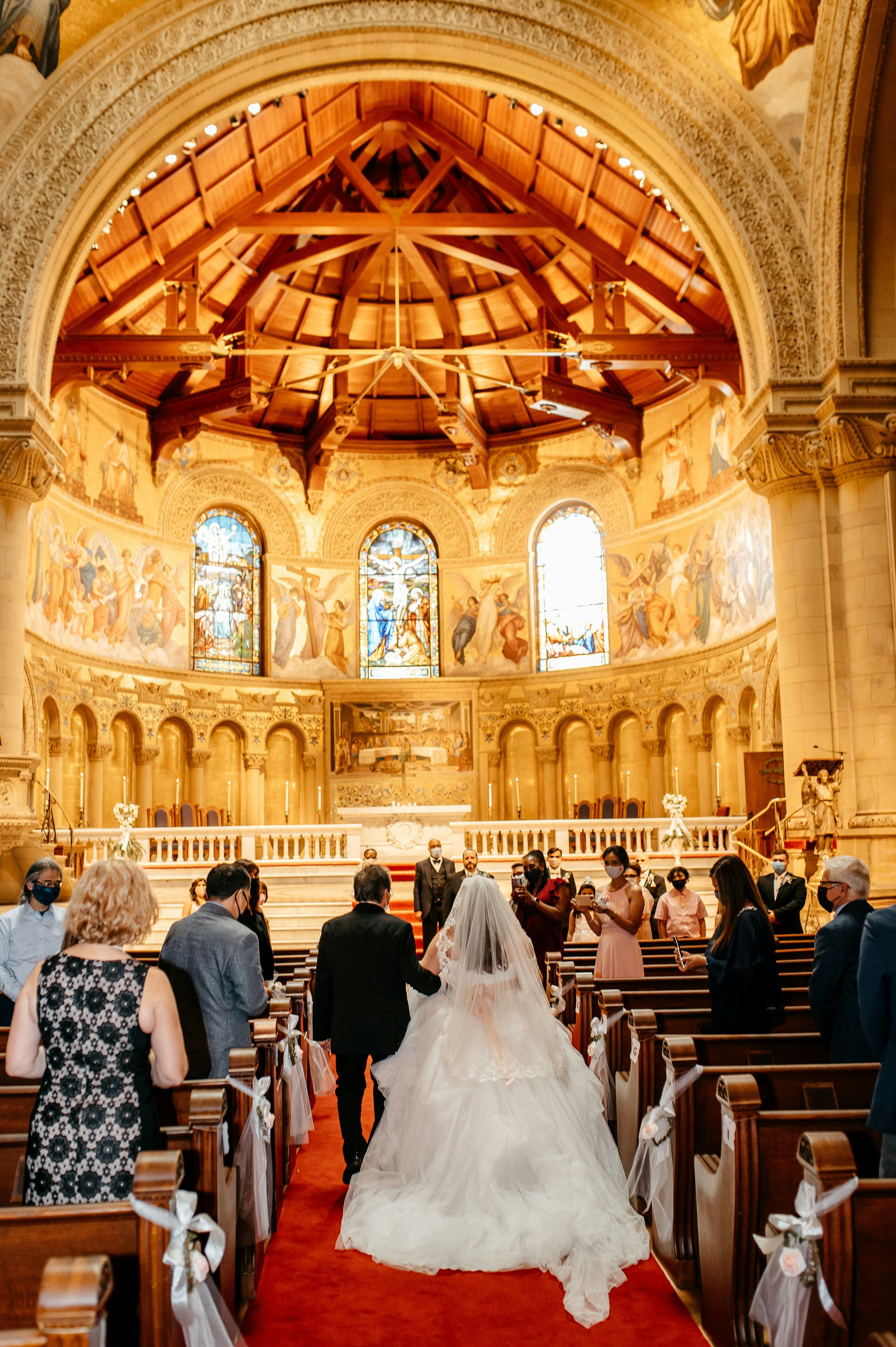 Bride walking down church aisle during wedding ceremony with guests seated`