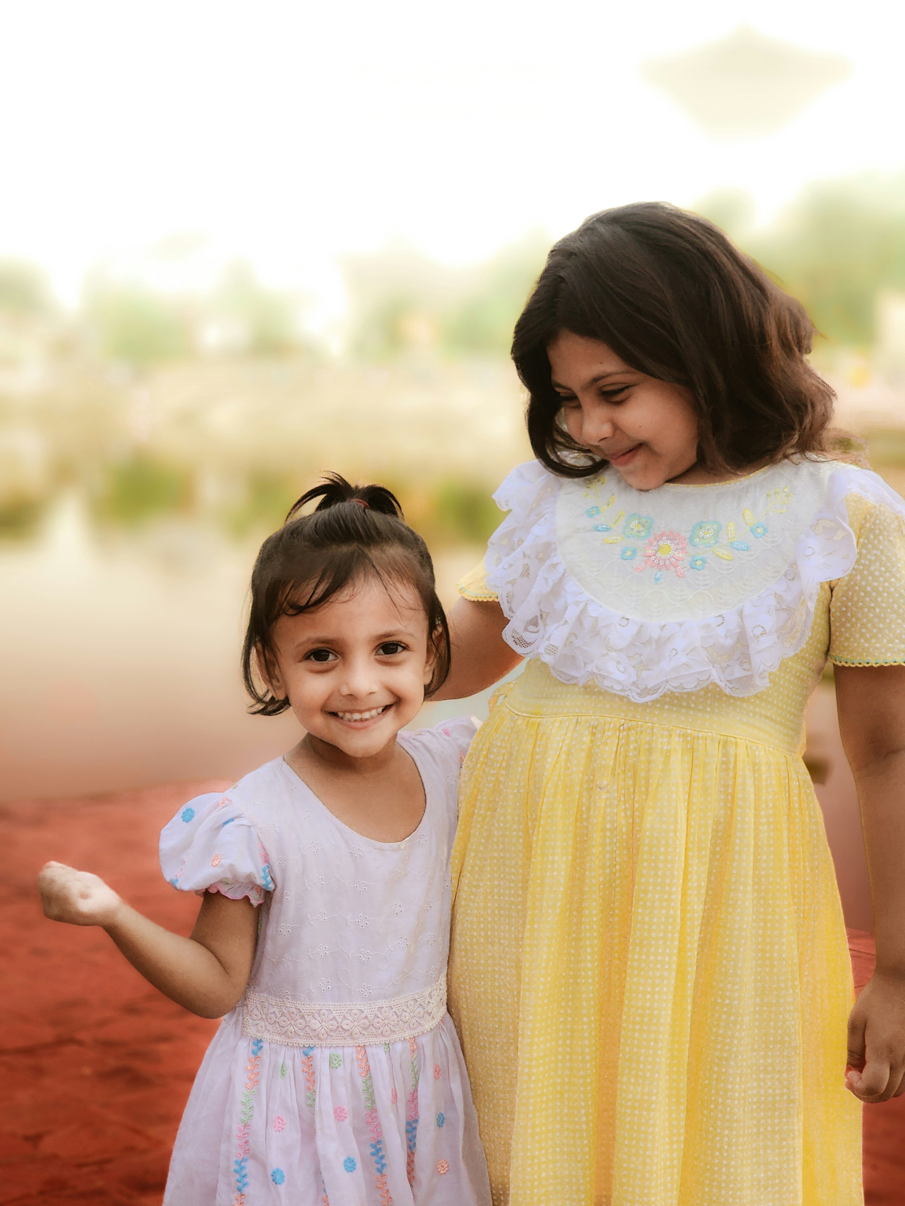 Two young girls in dresses smiling outdoors.
