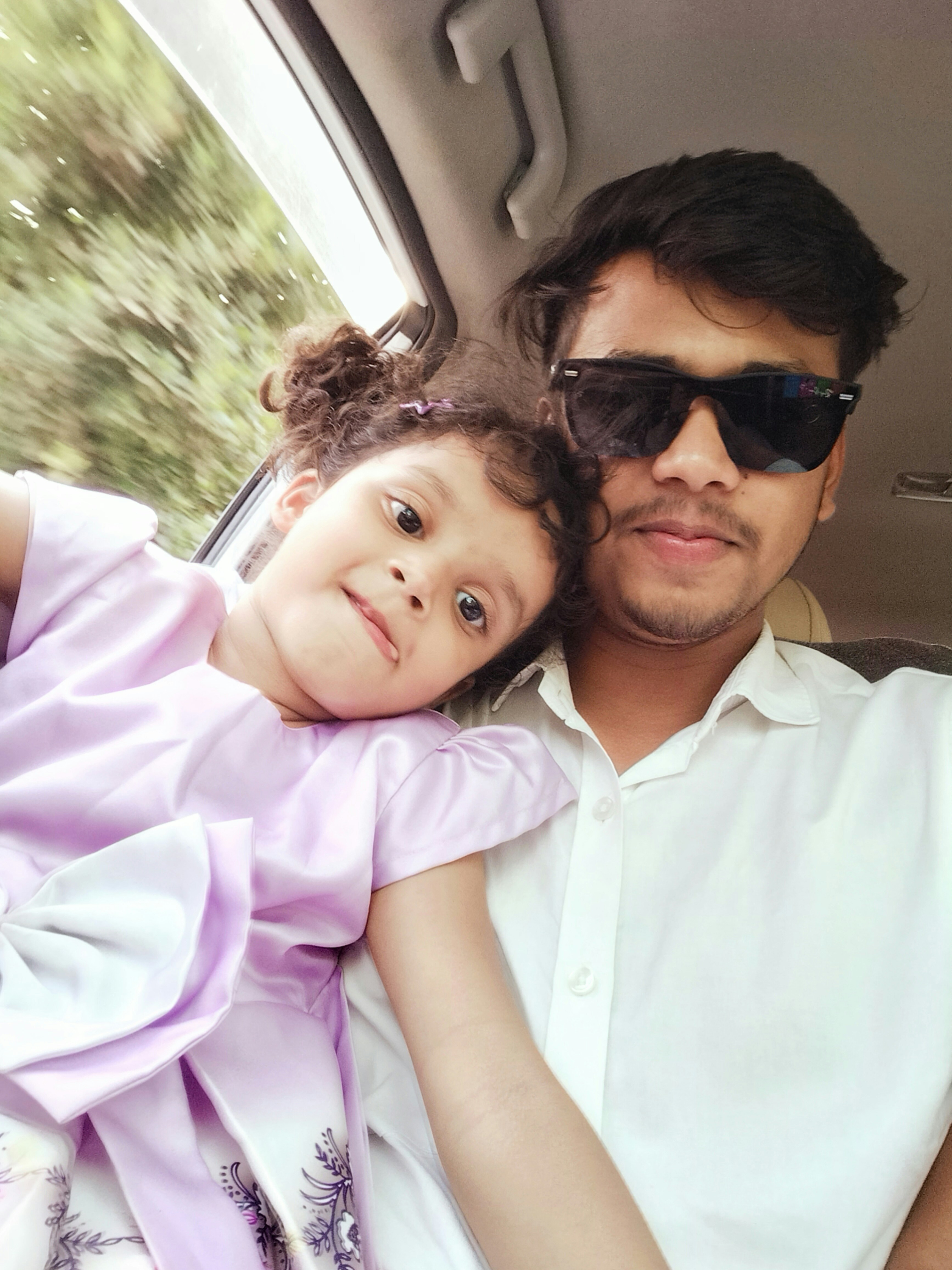 Young girl leans on man in sunglasses inside car