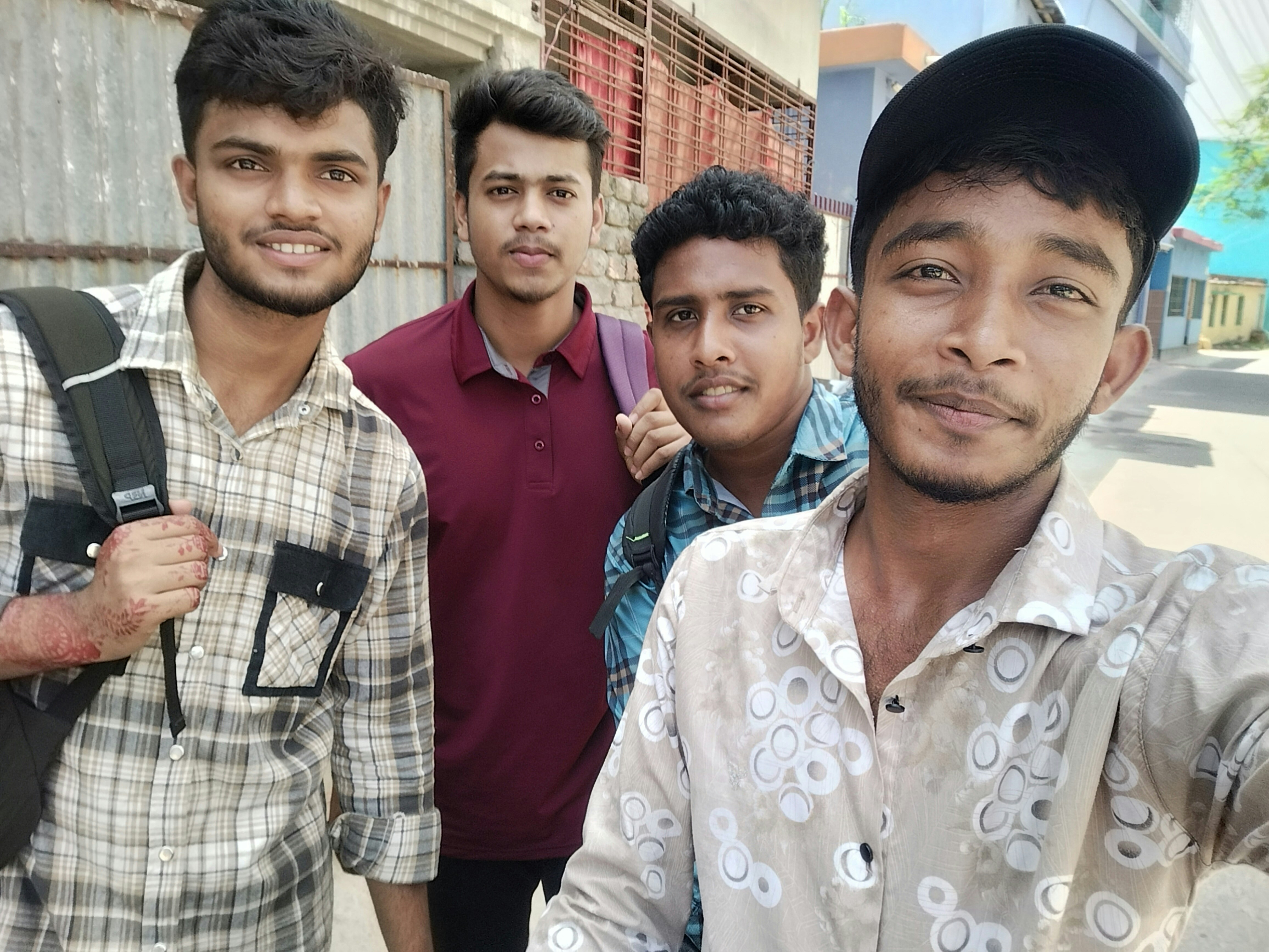 Four young men smiling and posing for a selfie outdoors.