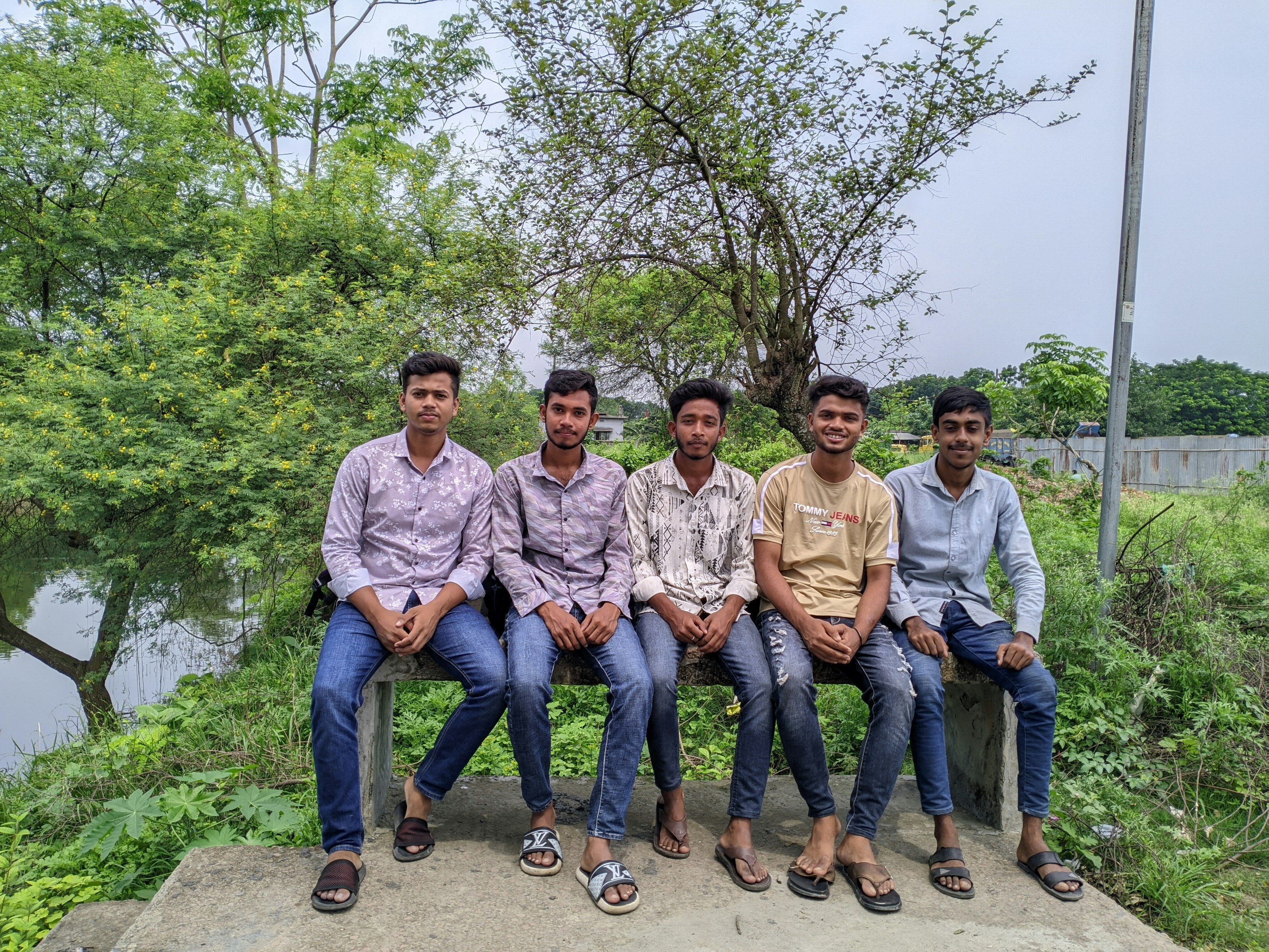 Five young men sitting outdoors with trees and water