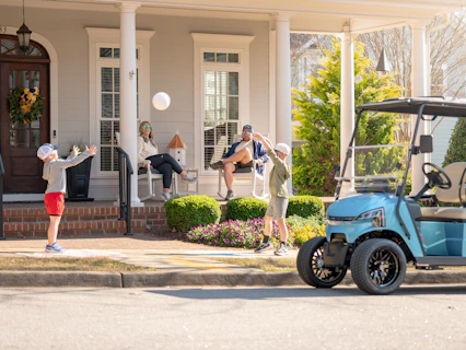 Two boys play ball near a golf cart and adults.