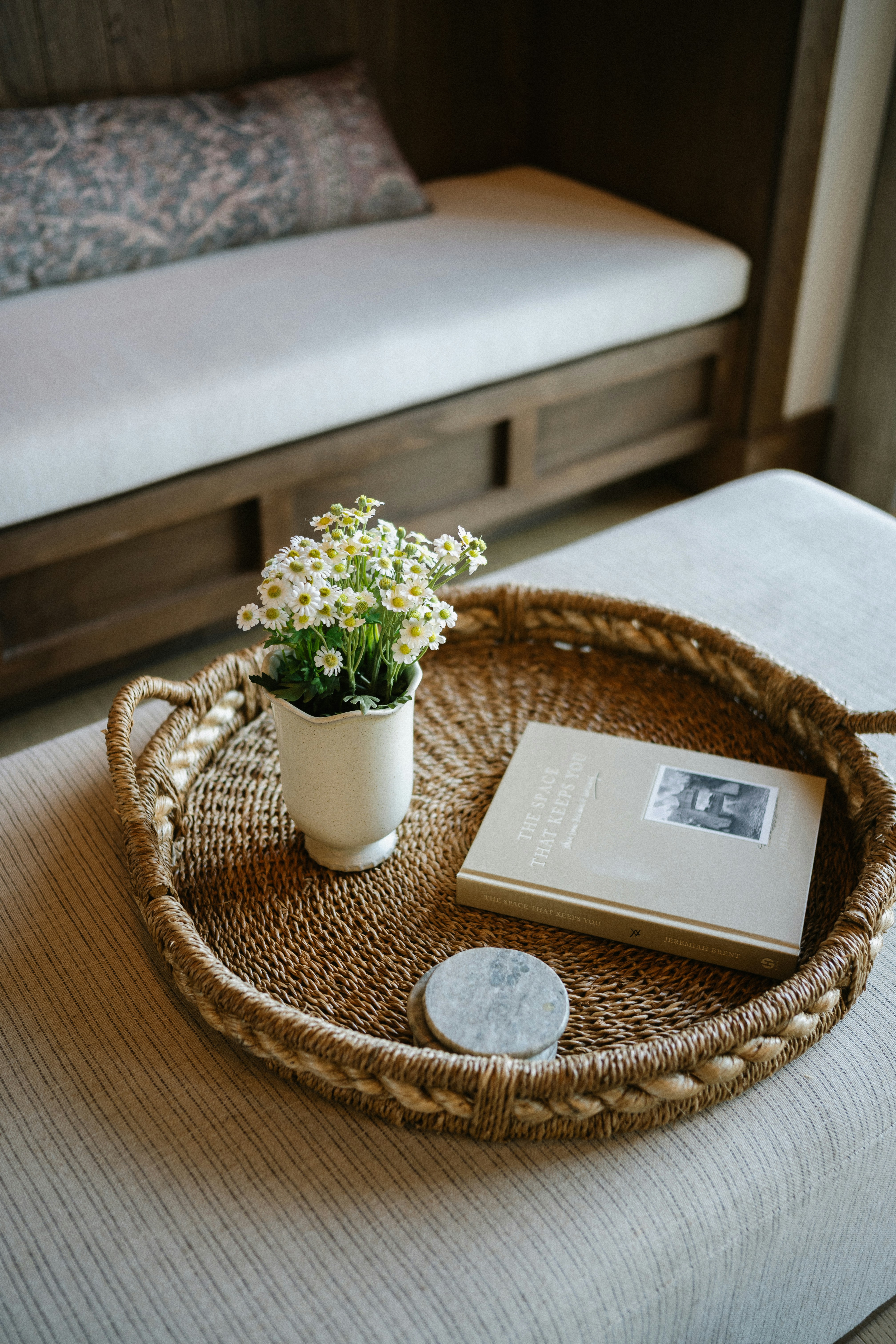 Woven tray with plant, book, and coaster on an ottoman.