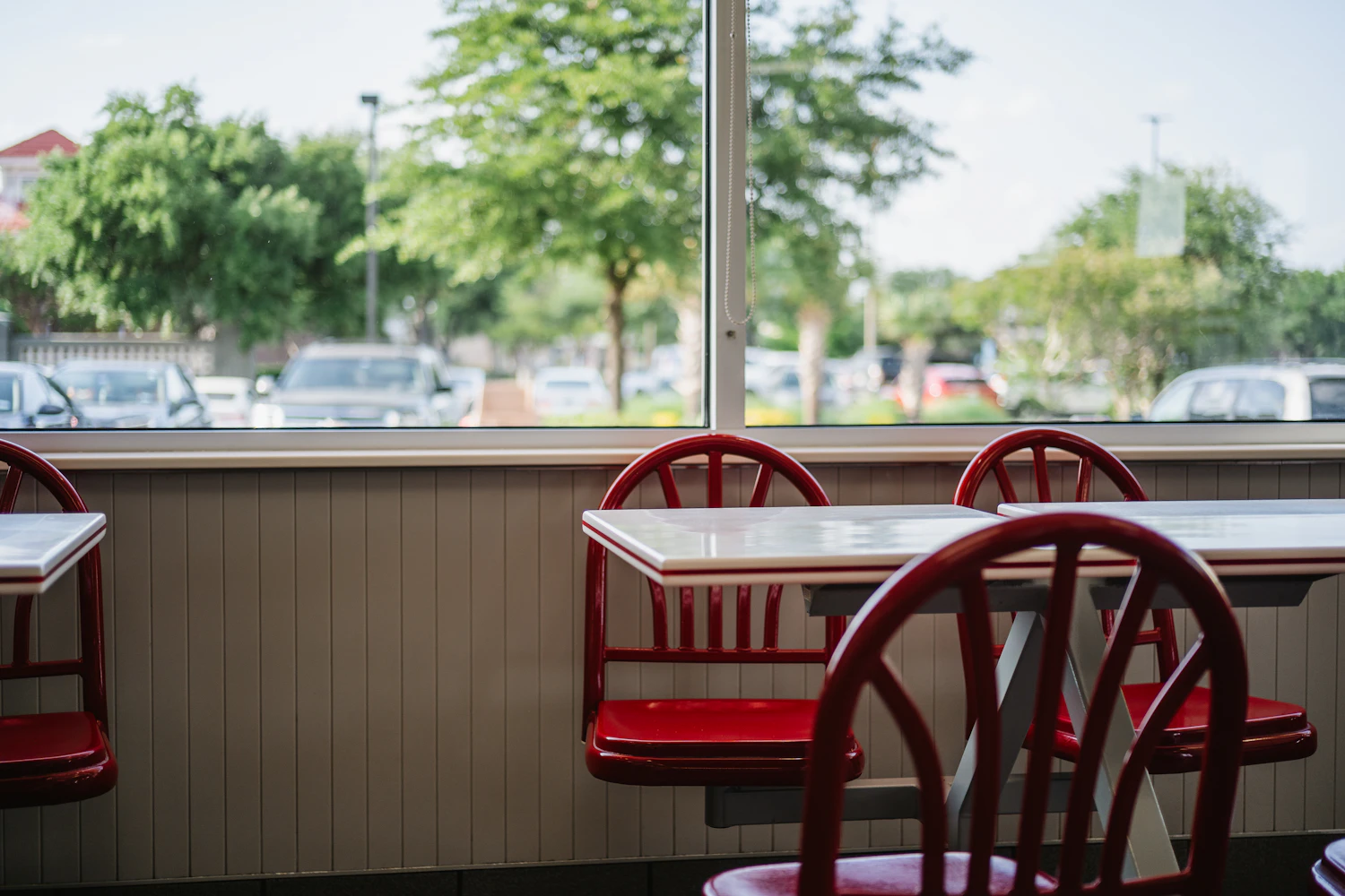 Red diner chairs and tables beside a window looking onto a car park