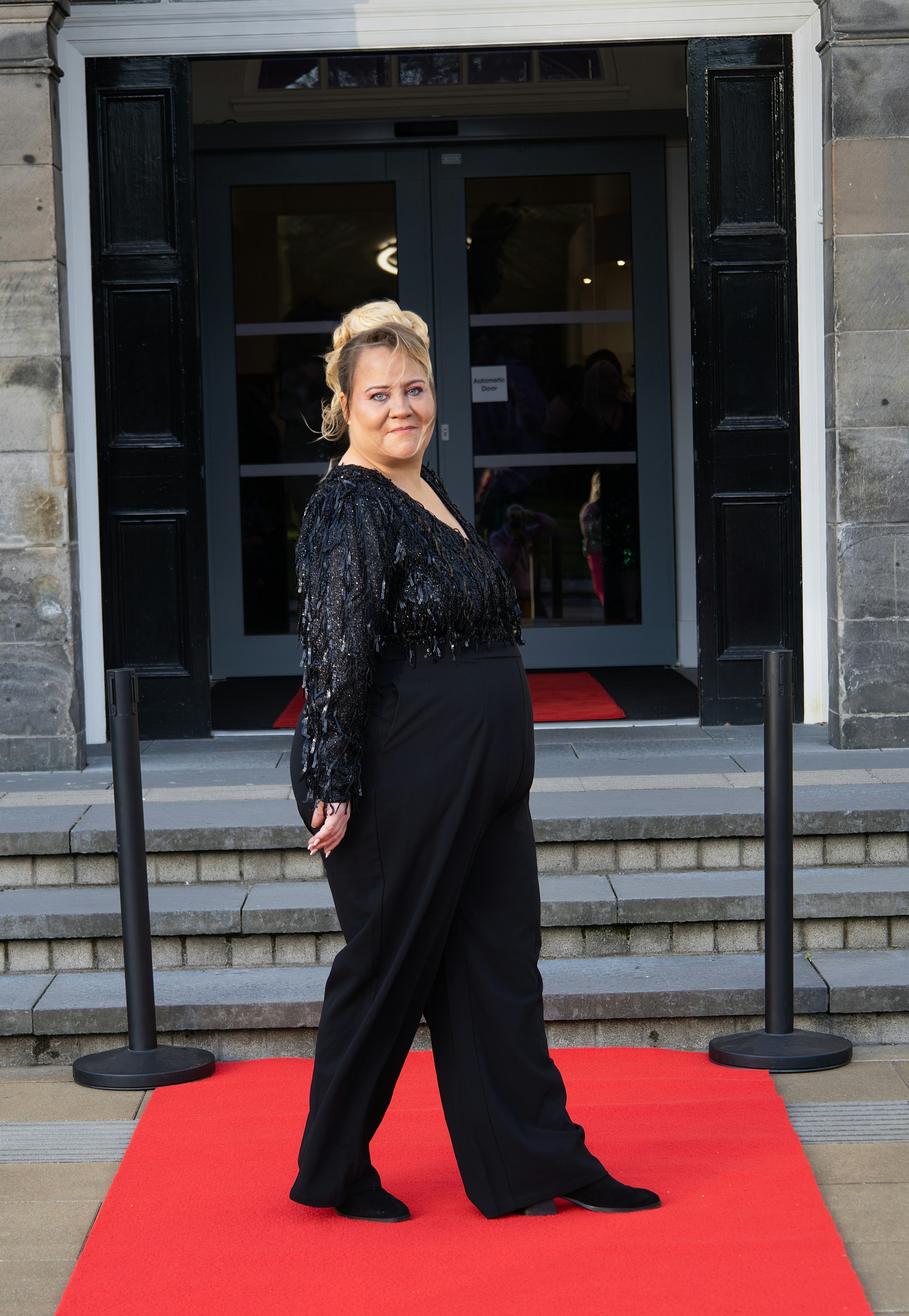 Une femme en noir pose sur un tapis rouge.