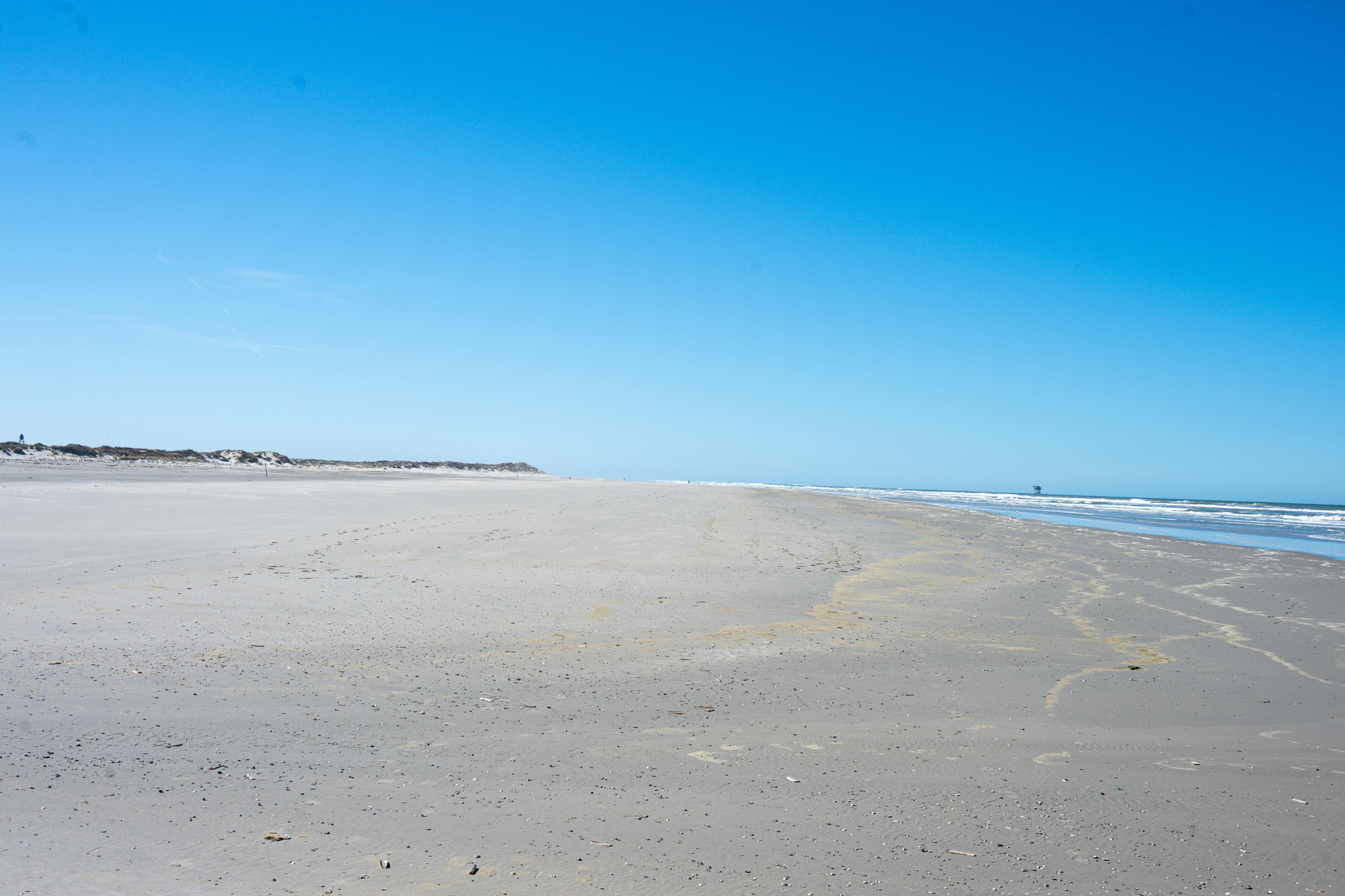 Vast empty sandy beach under a clear blue sky.