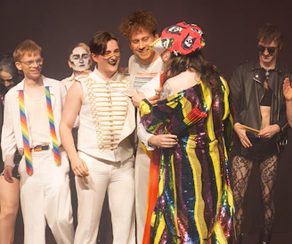 Diverse group of performers in vibrant costumes embracing on stage