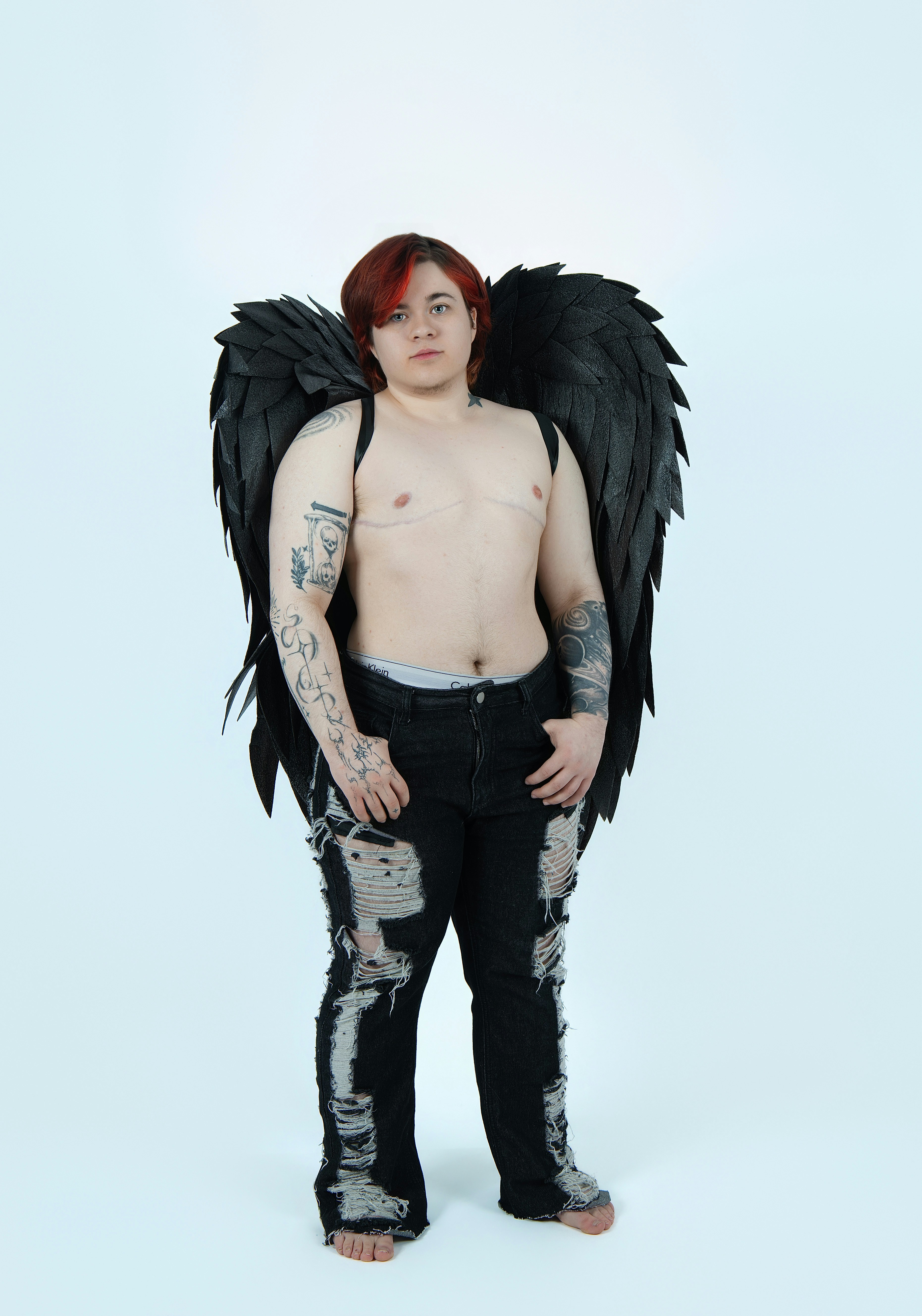 Orang dengan rambut merah, sayap hitam, dan celana jeans robek.