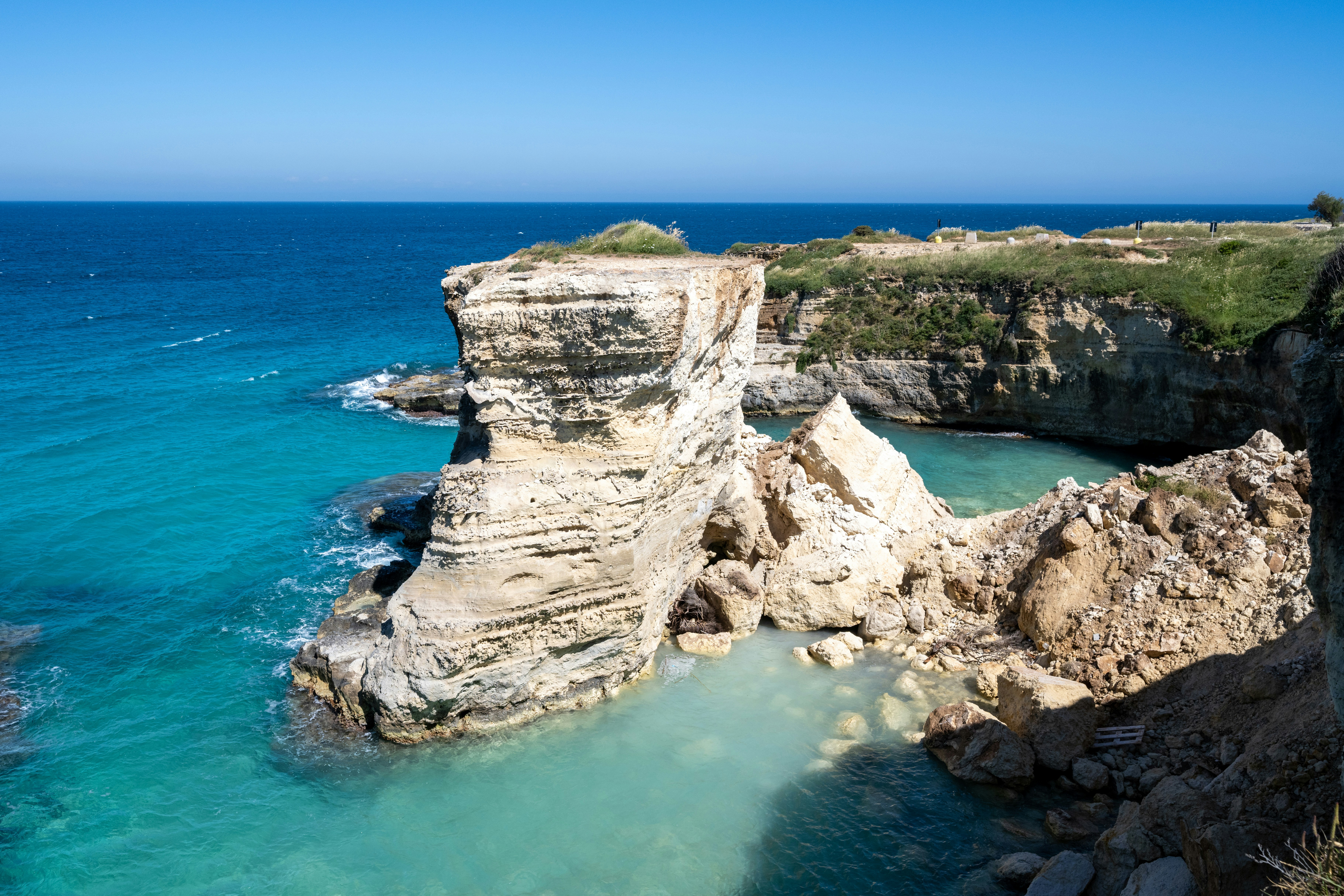 Coastal rock formations meet clear blue and turquoise ocean.